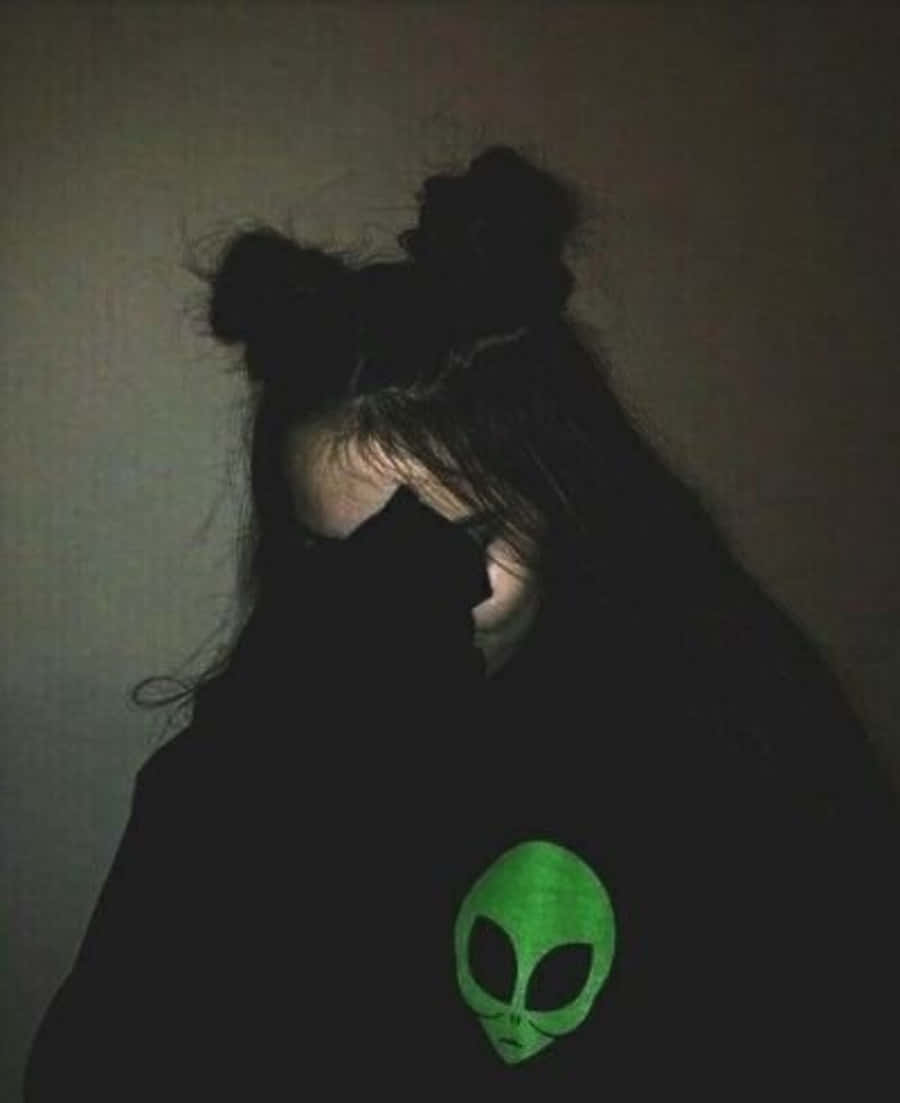 暗黑龐克 Tumblr 風格毛衣造型 壁紙 — 陰影中的人穿著黑色連帽衫，胸前有一個發光的綠色外星人頭，背景是昏暗的牆壁。