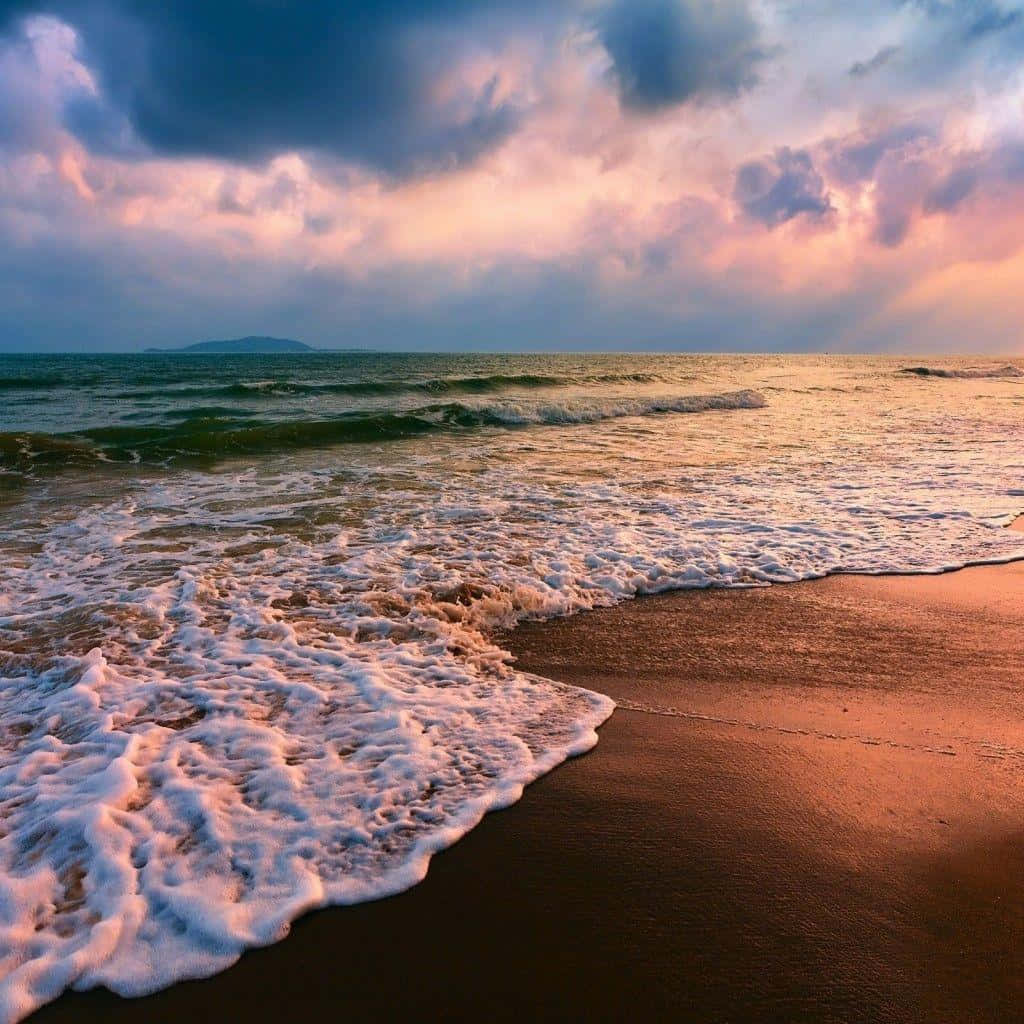 夕陽下，海浪湧向沙灘，上方是色彩斑斕的雲朵。