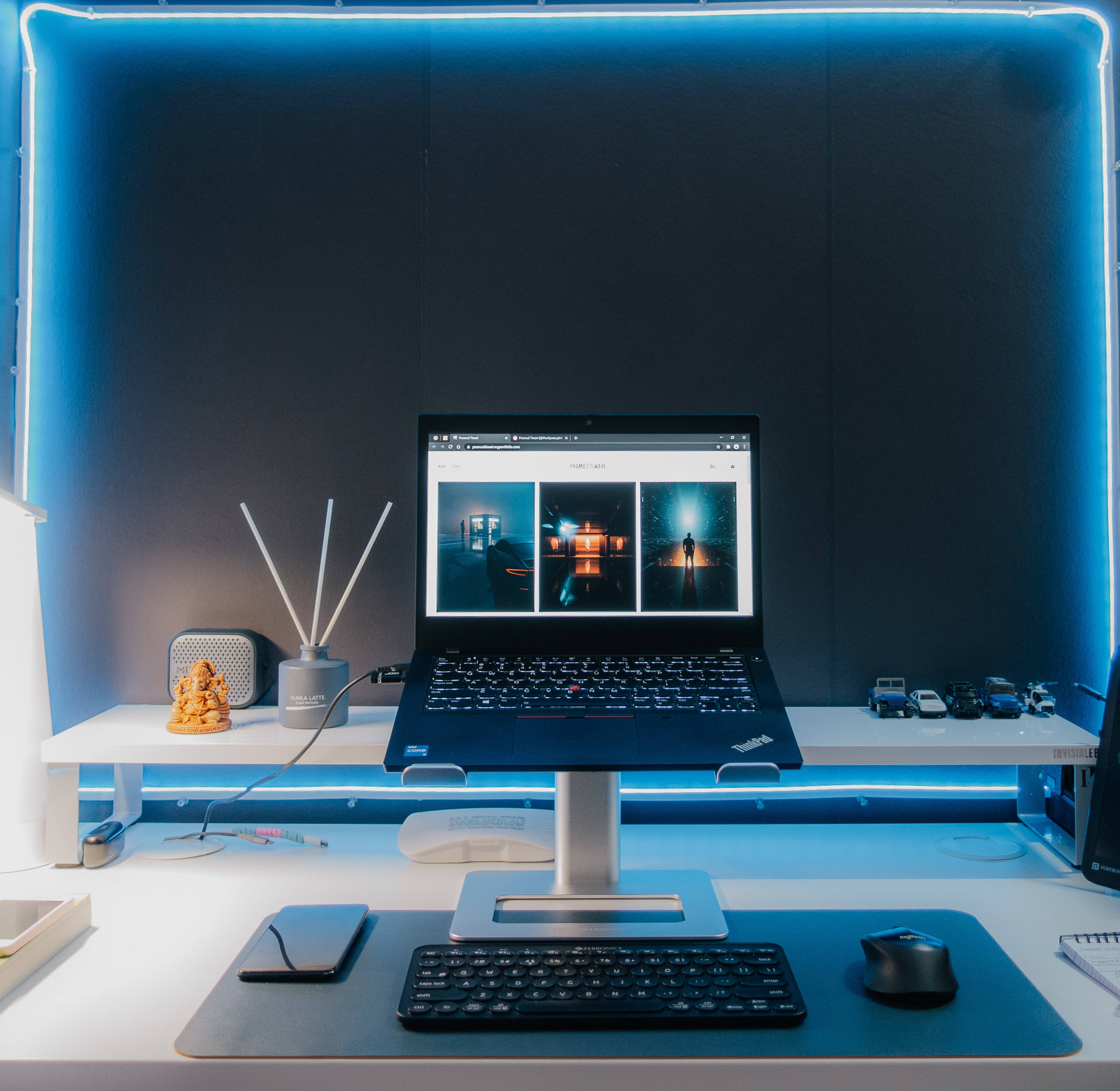 時尚Tumblr筆記本電腦藍光裝飾 壁紙 — 一部時尚的筆記型電腦放在支架上，顯示三個充滿氛圍的夜景，而發光的藍色霓虹燈框出一個簡約的白色桌面設置。