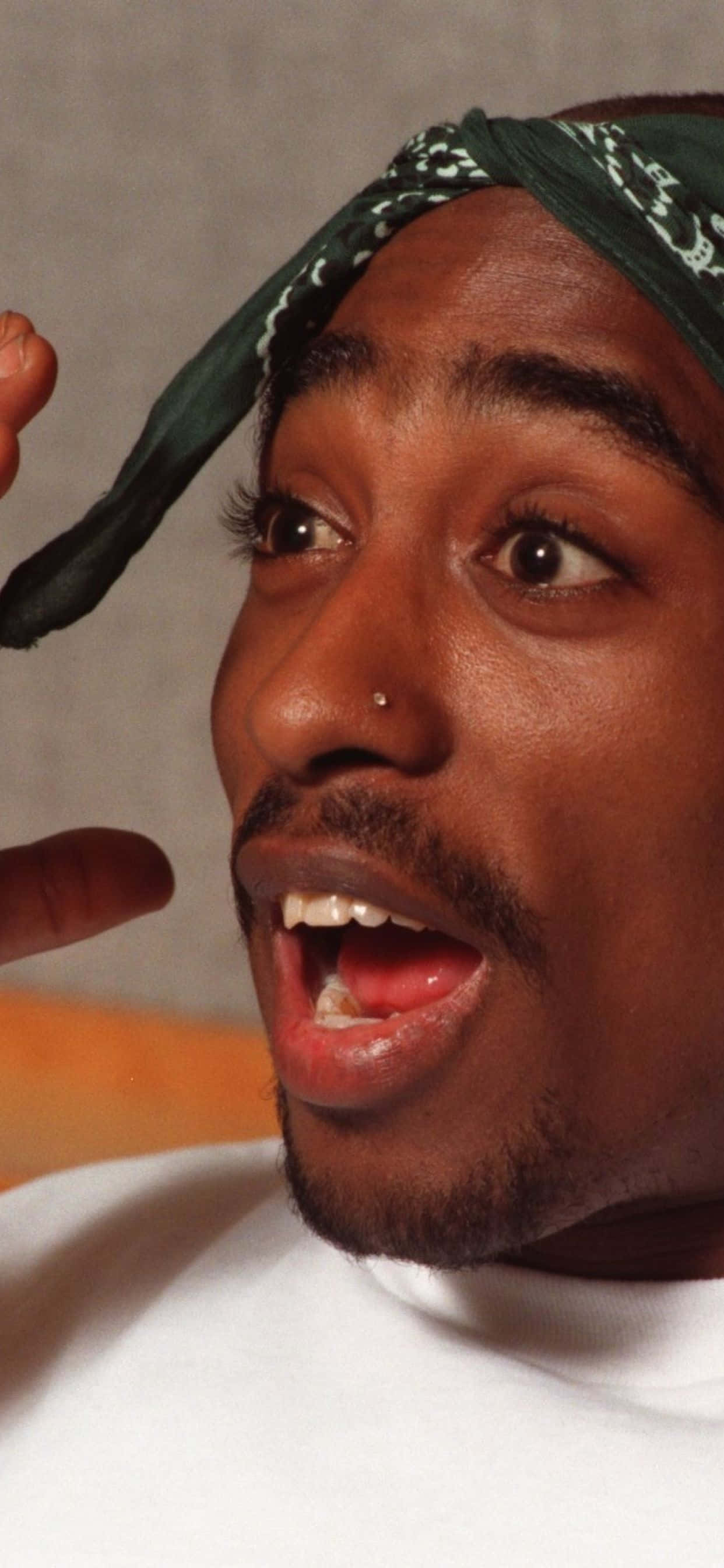 驚訝表情 Tupac iPhone 壁紙 — 一名戴著綠色頭巾、表情驚訝並做手勢的男子的特寫肖像。
