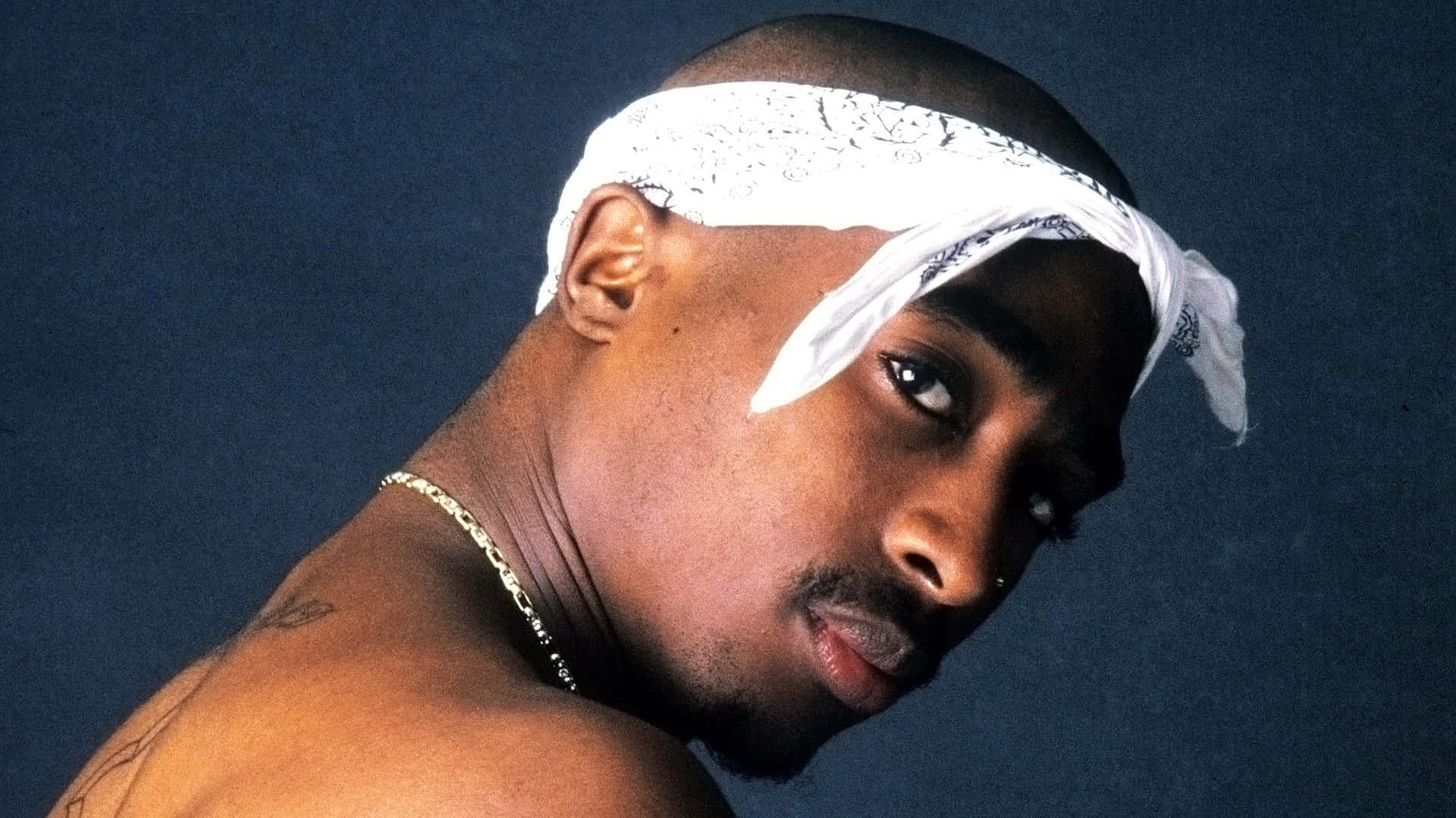 Tupac 桌布 壁紙 — Tupac Shakur 的頭像特寫，戴著白色頭巾和金鏈，背景為深藍色攝影棚。