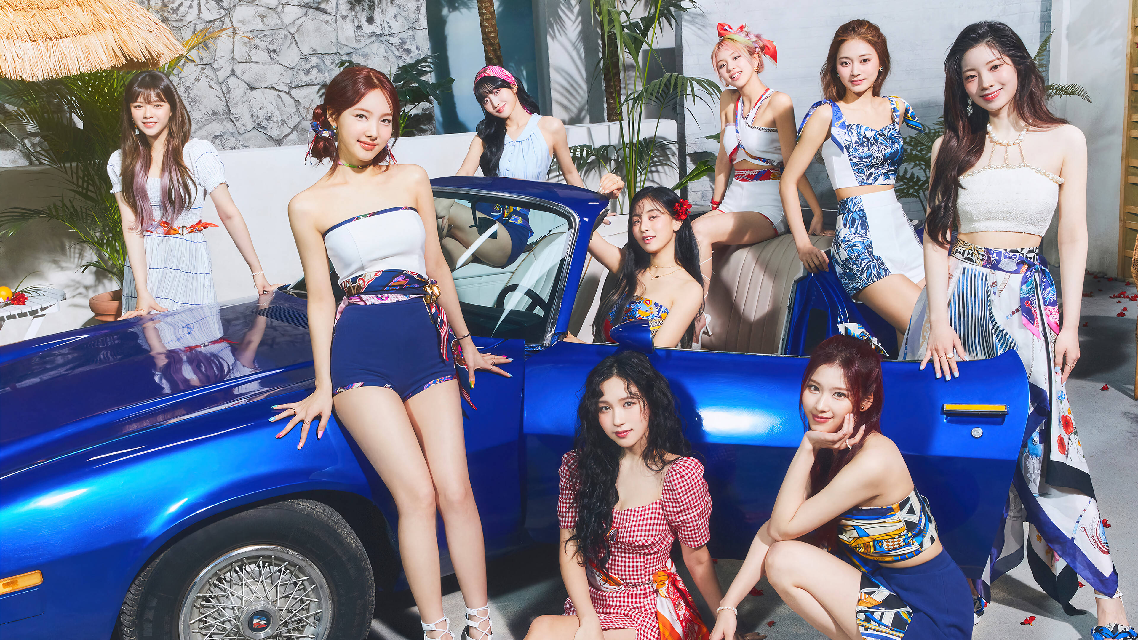 TWICE 4K 藍色豪華跑車背景 壁紙 — 七位時尚女性穿著色彩繽紛的復古服裝，在熱帶庭院中圍著一輛閃亮的藍色敞篷車俏皮地擺姿勢。
