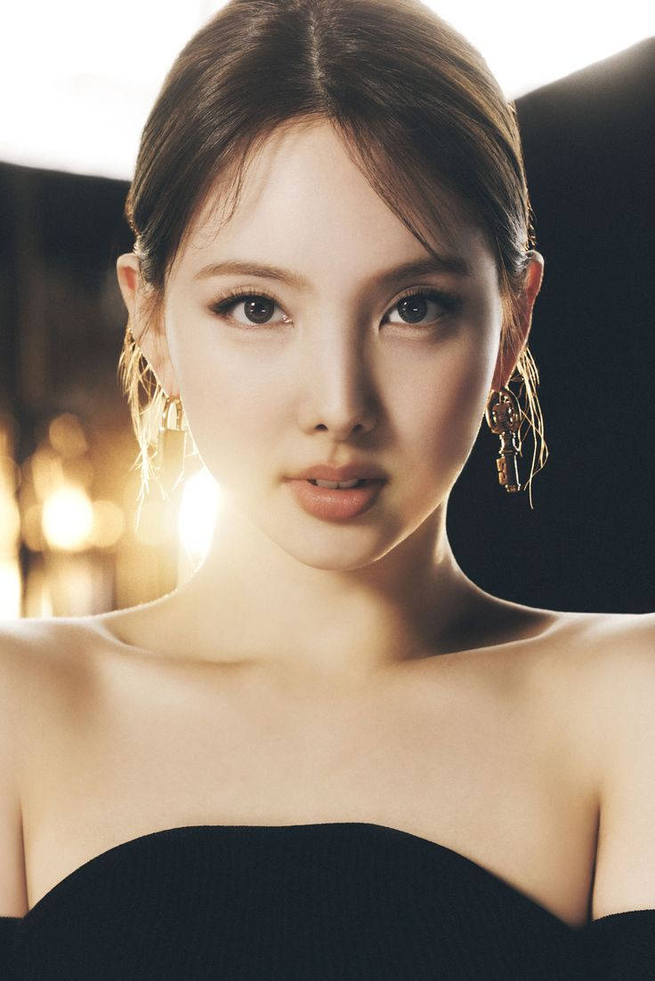 一位穿著黑色連衣裙、戴著金色耳環的女性在昏暗的攝影棚中看著相機。
