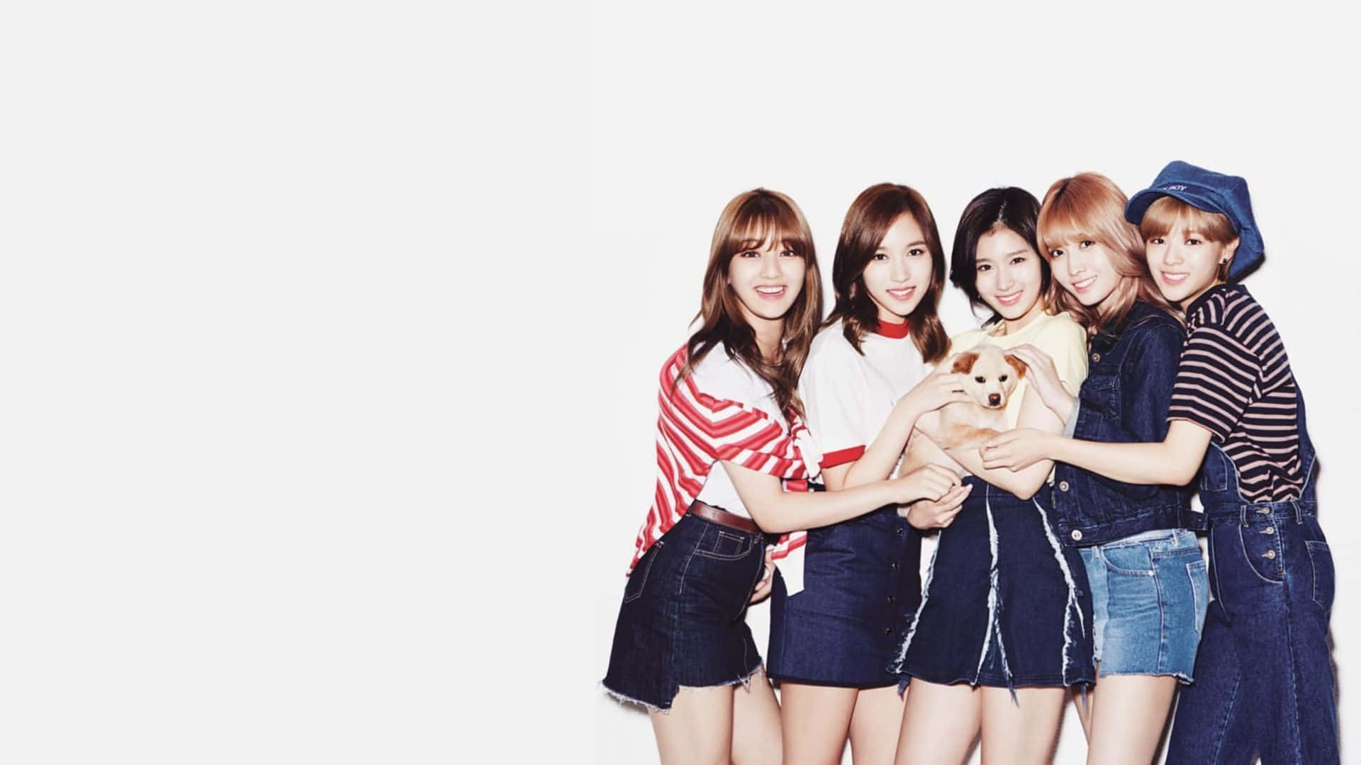 TWICE 快樂同框 壁紙 — 五位微笑的年輕女性穿著牛仔服裝，一起抱著一隻小狗，在純白色背景前擺姿勢。