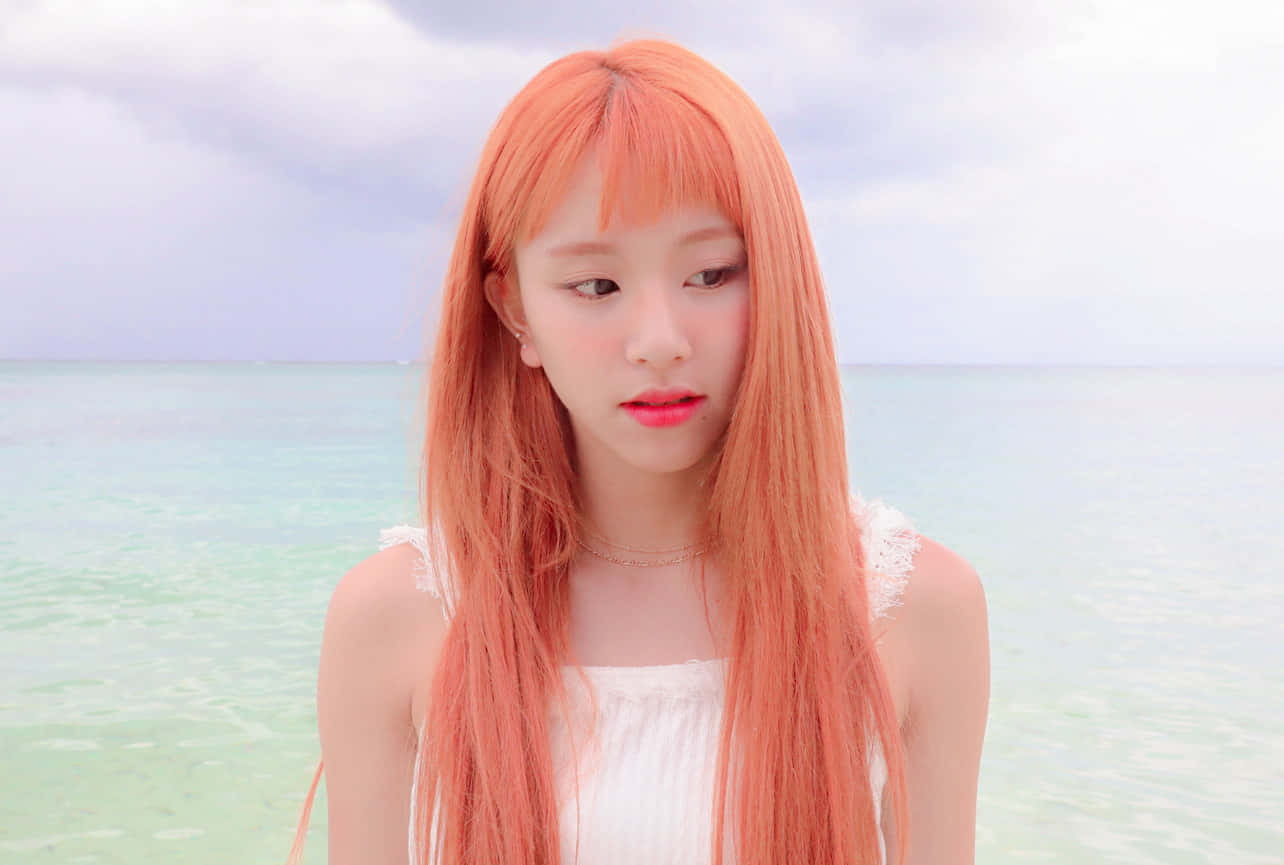 TWICE - 璀璨團體照 壁紙 — 一位年輕女子擁有充滿活力的桃色頭髮，站在平靜的碧綠海水旁，天空柔和多雲。