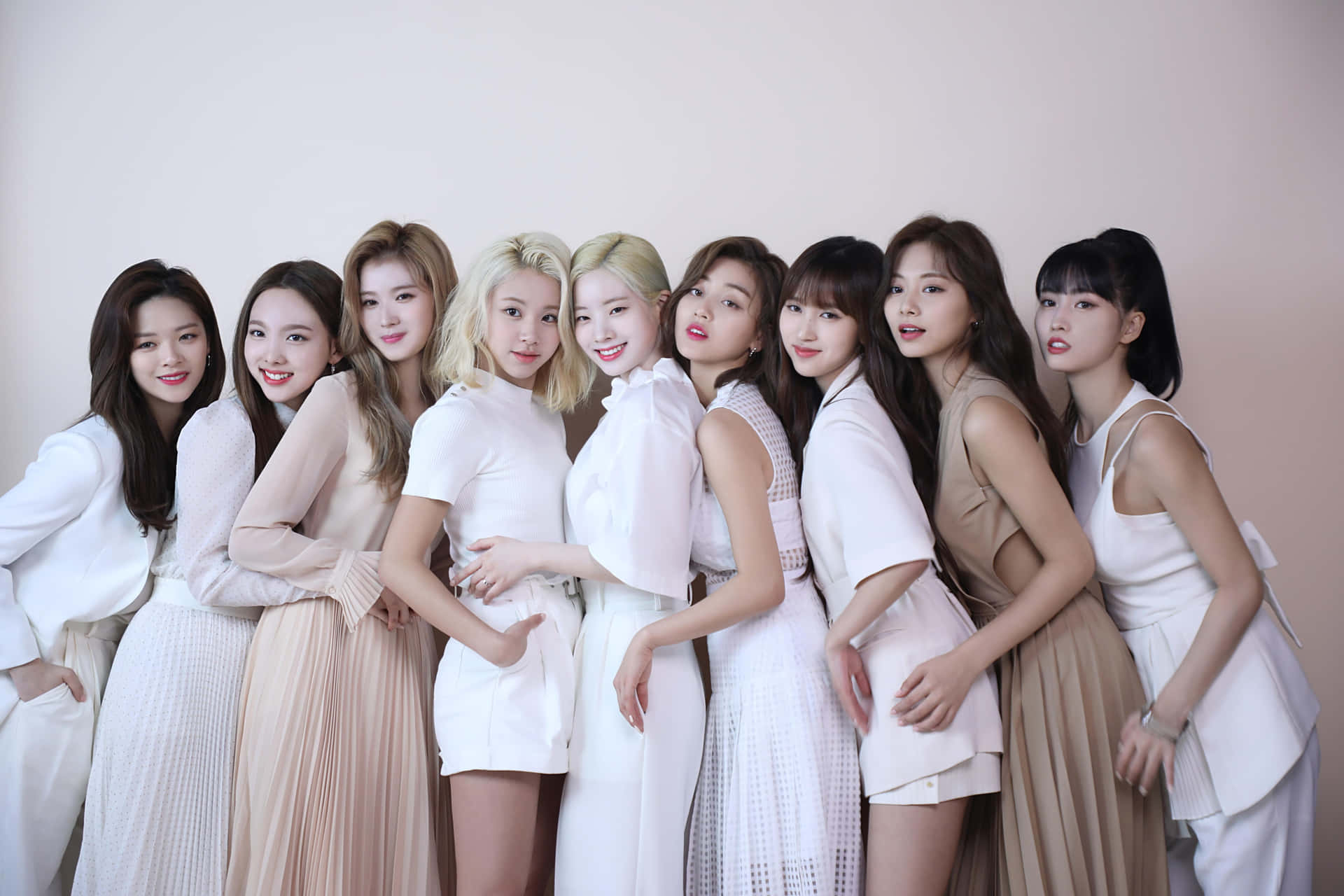 Twice 舞台炫目演出 壁紙 — 八位時尚女性身穿白色和米色服裝，在柔和的粉紅色背景前緊密地擺姿勢。
