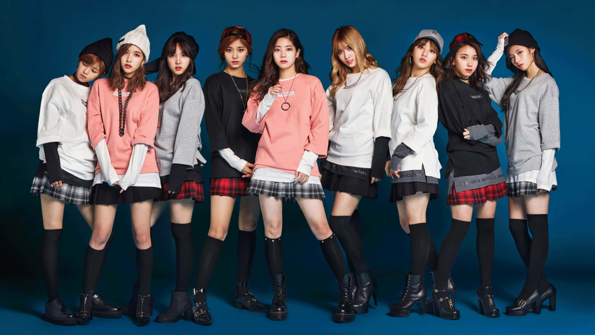 TWICE成員志效、Tzuyu、Momo、Sana與彩英展現迷人風采！ 壁紙 — 八位時尚年輕女性穿著搭配的毛衣、格子裙和黑色靴子，在純藍色攝影棚背景前自信地擺姿勢。