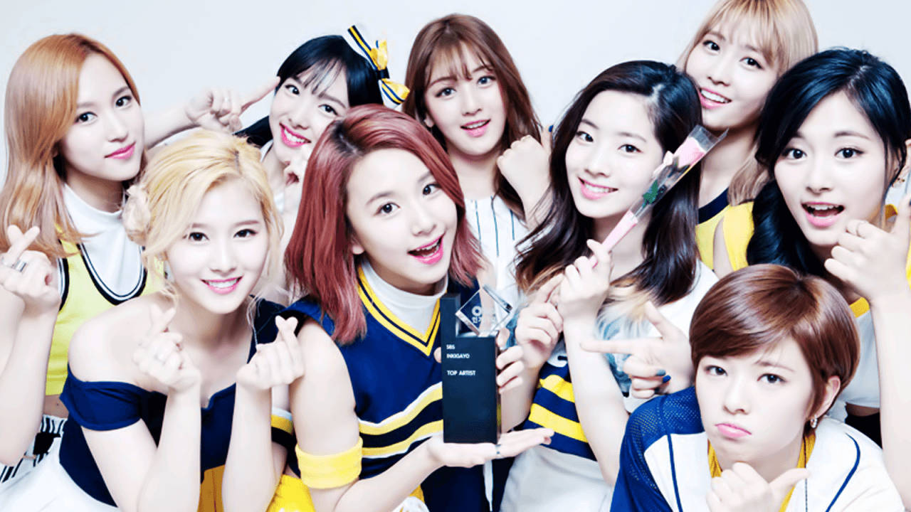 K-pop 女子組合穿著啦啦隊服裝，手持獎項獎盃並對著鏡頭擺姿勢。