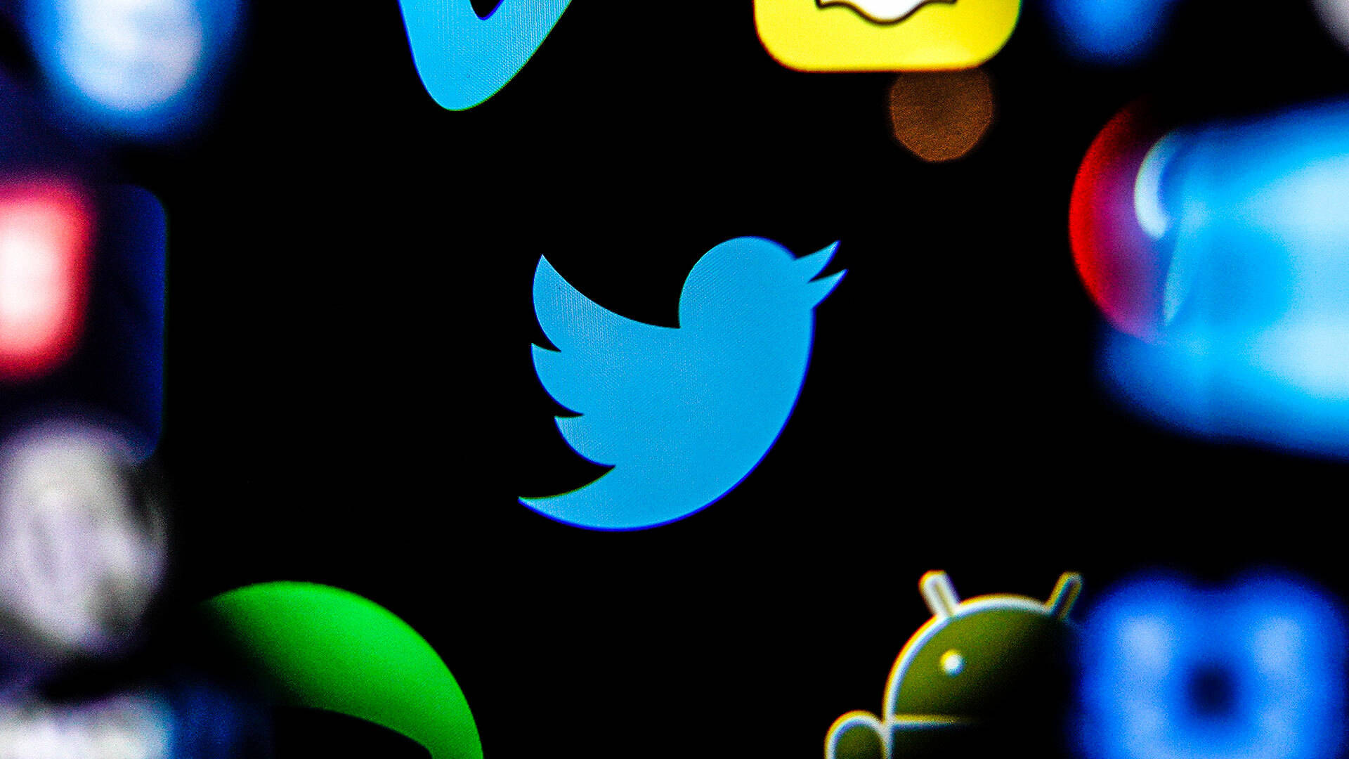 Twitter社交媒體應用程式 壁紙 — 暗色屏幕上模糊應用程式圖標中，一個發光藍色Twitter鳥圖標的特寫。