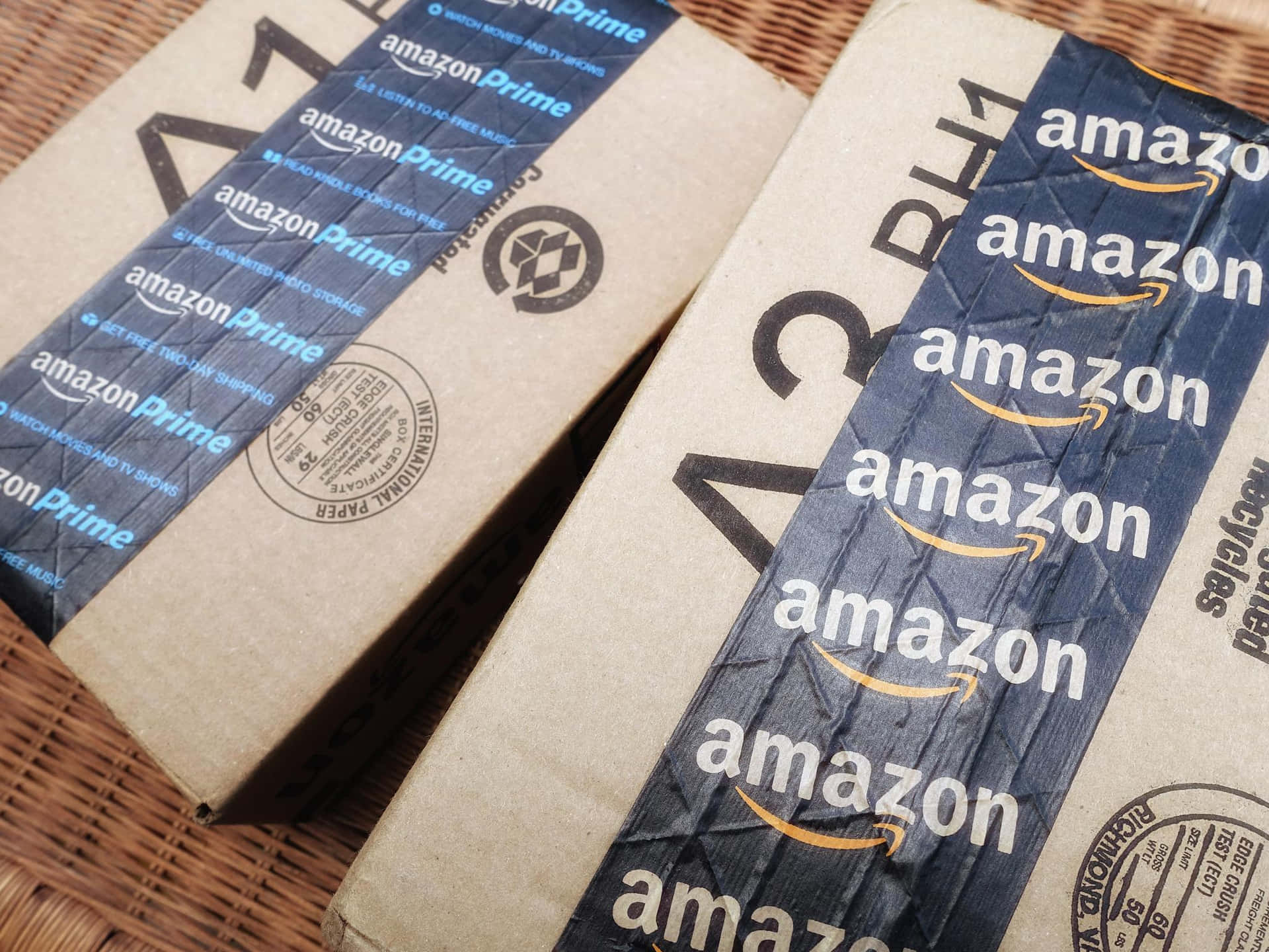  壁紙 — 兩個皺巴巴的Amazon Prime紙箱放在編織柳條表面上，帶有可見的運送標籤和標誌。