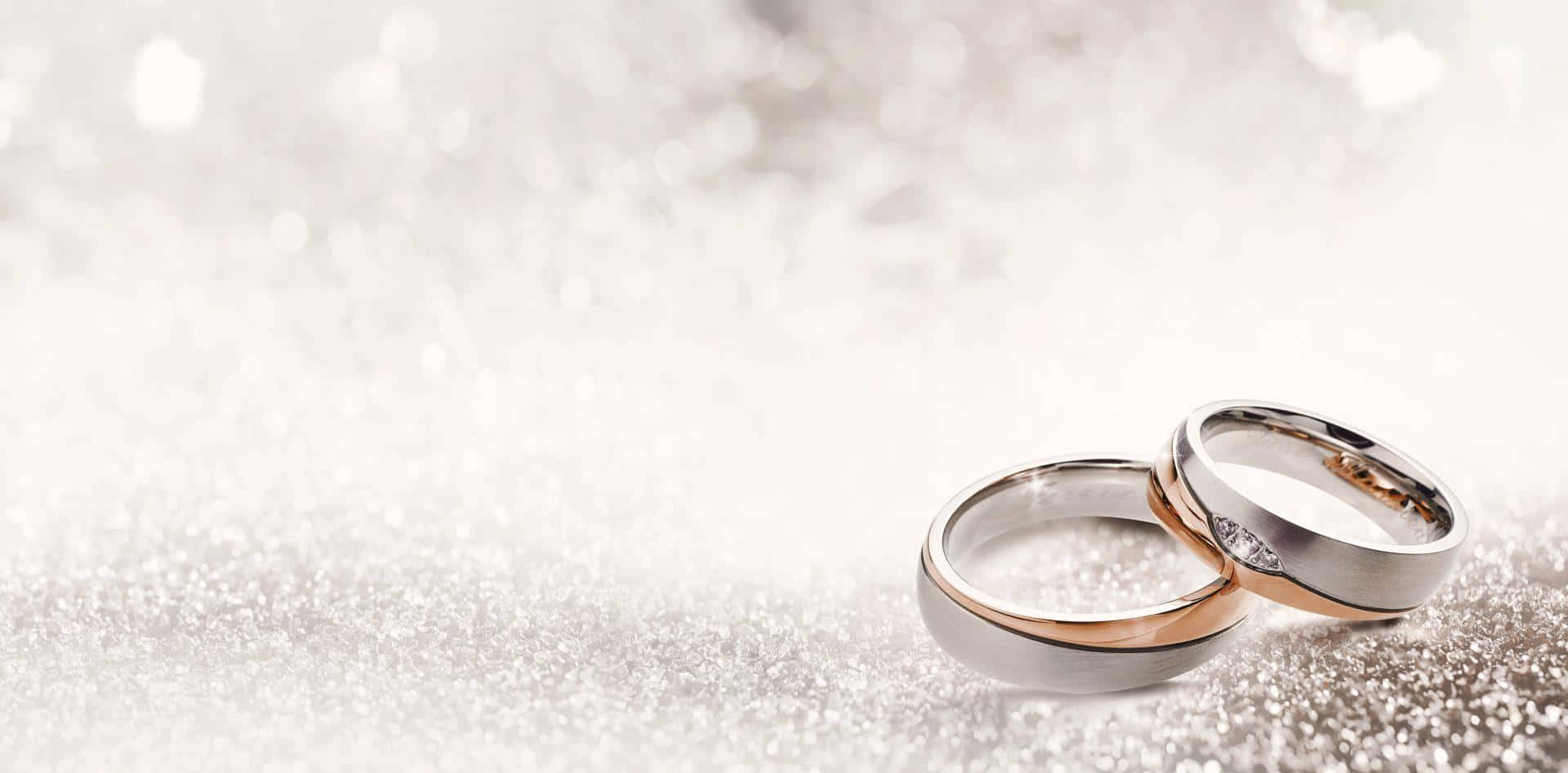 兩枚結婚戒指，一枚玫瑰金一枚銀色，在閃爍的銀色表面上。