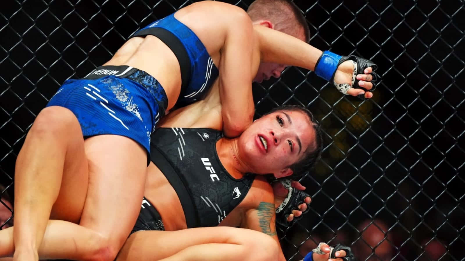  壁紙 — 兩名女性MMA拳手在八角籠內激烈纏鬥，其中一人施展鎖喉技。