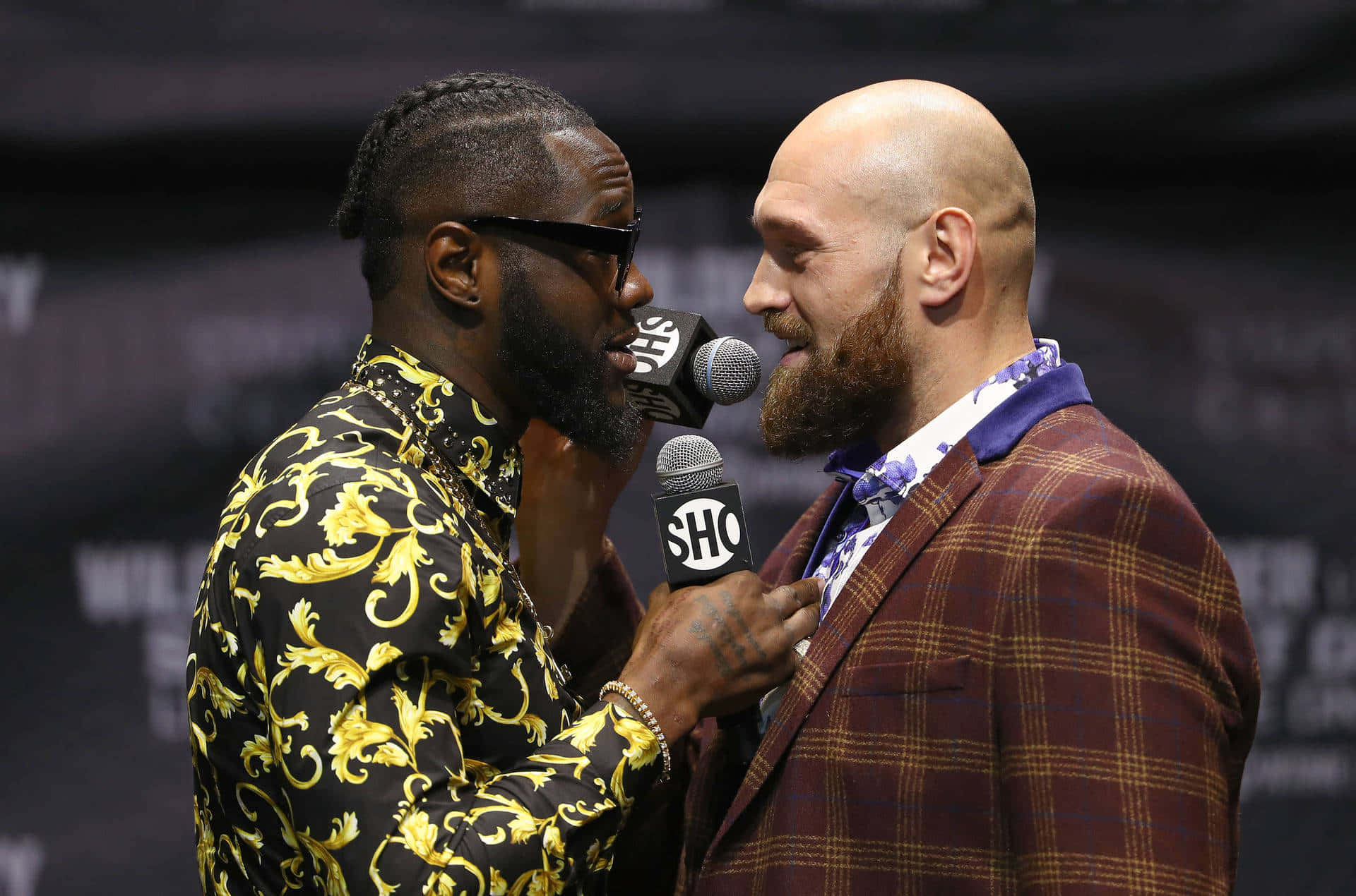  壁紙 — 兩名拳手在記者會上激烈對峙，一人手持麥克風，另一人穿著大膽圖案襯衫。