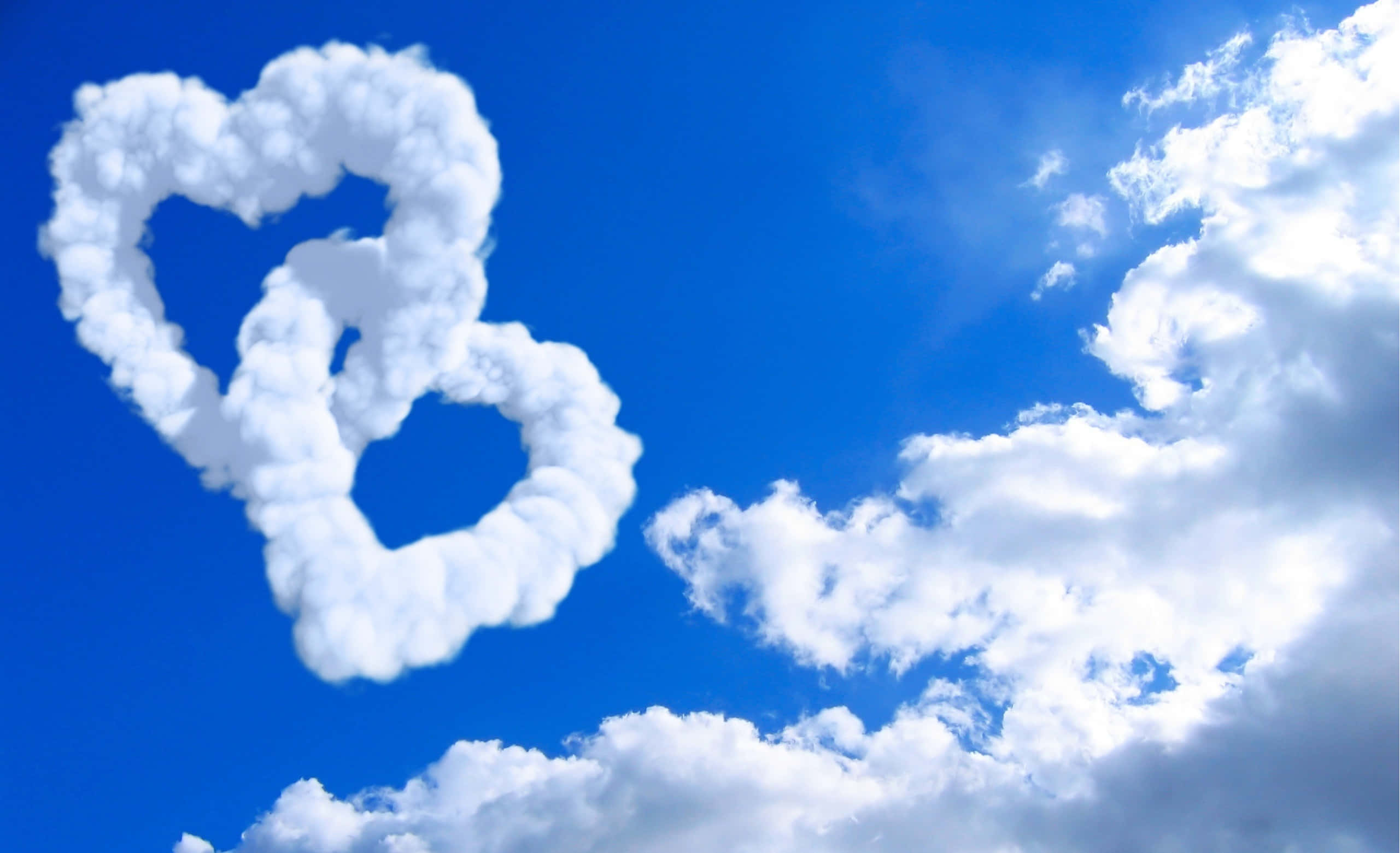 I Love God 桌布 壁紙 — 兩朵蓬鬆白色心形雲朵漂浮在蔚藍天空中，伴隨著散落的縷縷雲絲。
