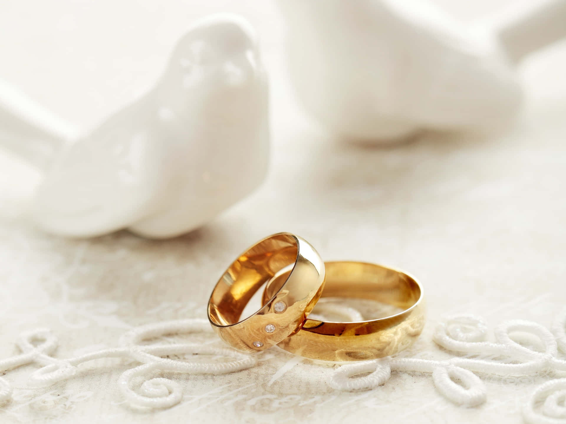 白色蕾絲上的兩枚帶鑽石的金色結婚戒指，旁邊是陶瓷鴿子。