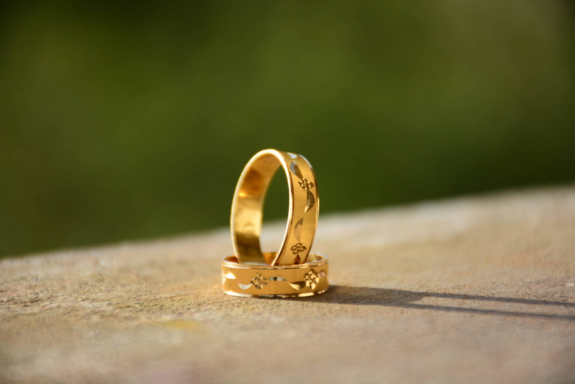 自然光下，木質表面上兩枚帶有花卉圖案的金色結婚戒指。