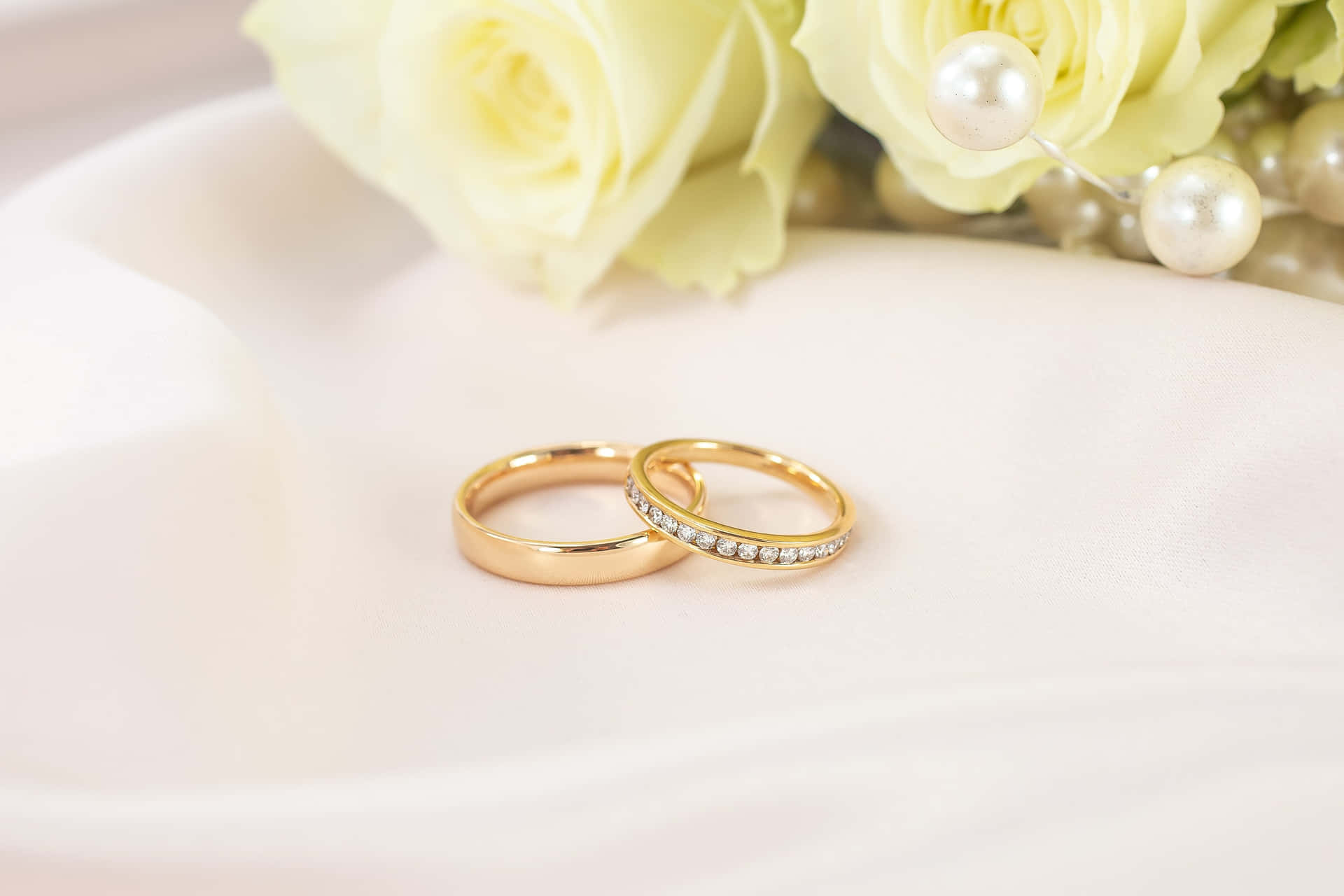 兩枚金色結婚戒指，配以珍珠和黃色玫瑰，置於白色布料上。