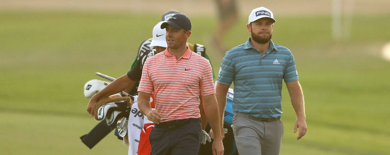 Tyrrell Hatton 桌布 壁紙 — 兩名身穿條紋襯衫的男性高爾夫球手在陽光明媚的綠色球場上行走，球童在他們身後攜帶球桿。