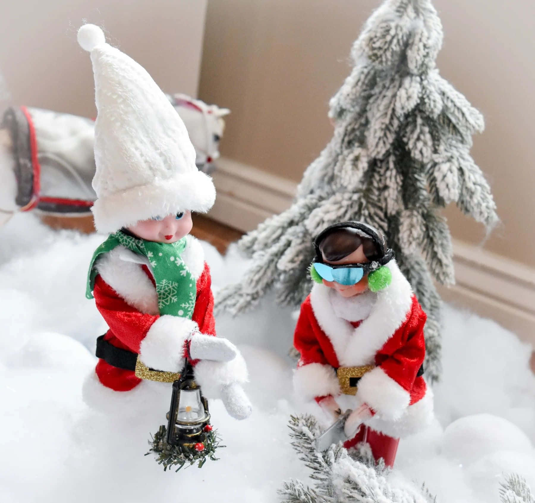  壁紙 — 兩個迷你聖誕老人公仔在雪景中，一個拿著燈籠，另一個戴著護目鏡，旁邊是結霜的樹。