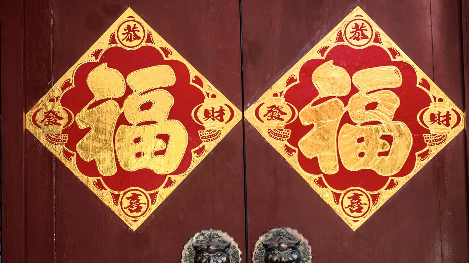  壁紙 — 兩副華麗的紅色和金色中國新年春聯裝飾著一扇帶有獅頭門環的深色木門。