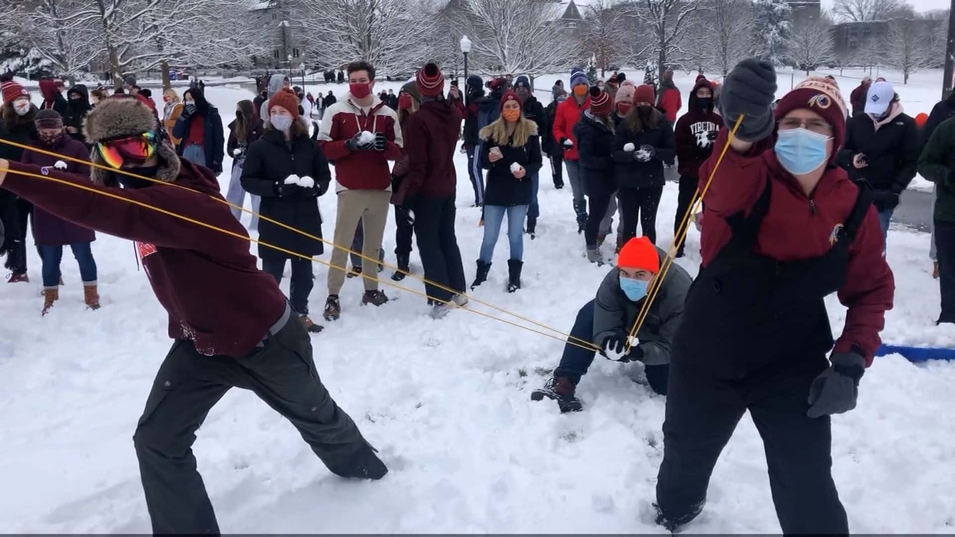 壁紙 — 兩人在栗色外套中拉著雪繩，而人群在雪地公園觀看。