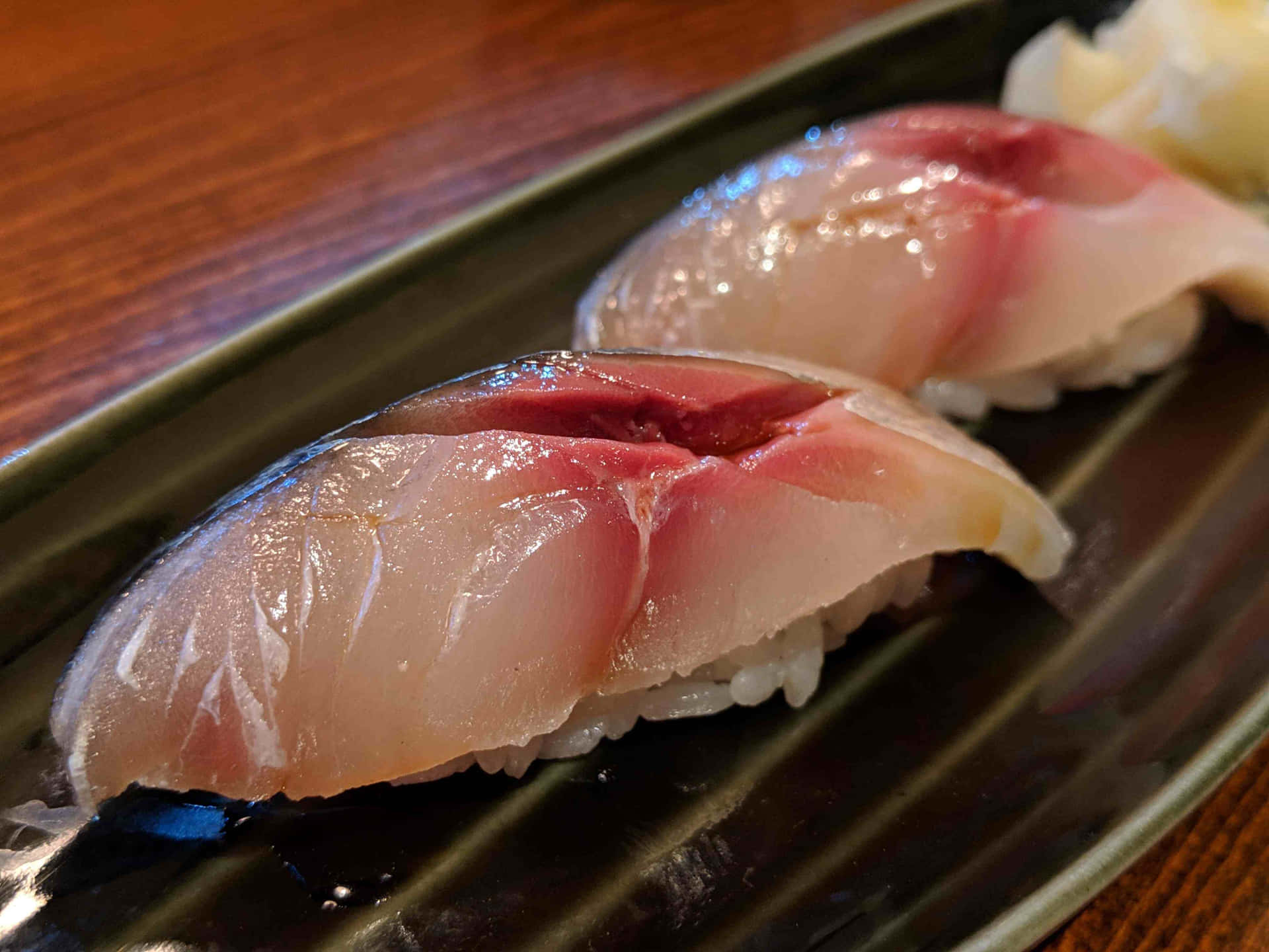  壁紙 — 兩件新鮮吞拿魚握壽司在深綠色碟子上閃閃發光，旁邊有芥末。