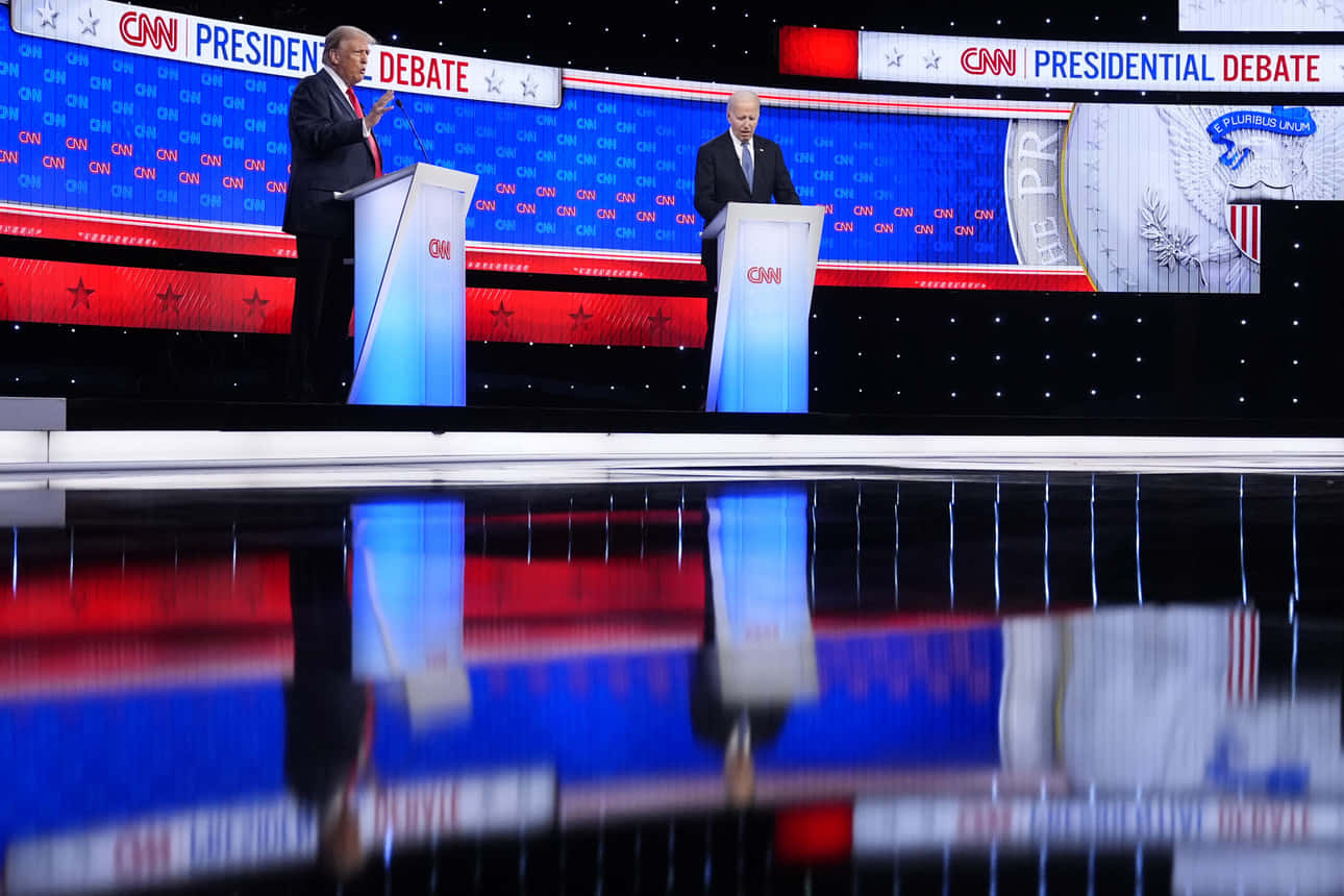  壁紙 — 兩位總統候選人站在CNN辯論舞台的講台上，愛國紅、白、藍燈光在光澤地板上反射。