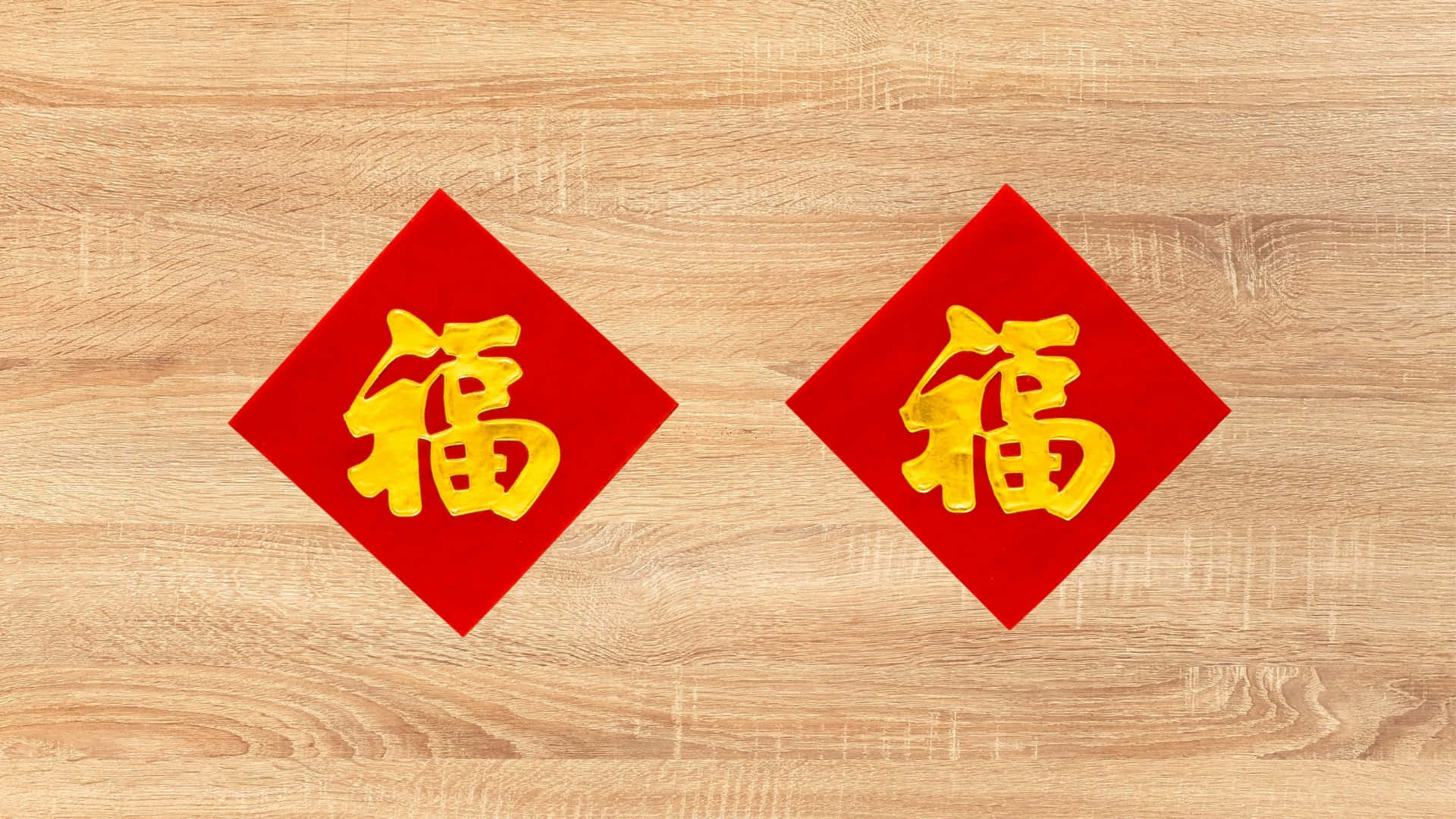  壁紙 — 兩個紅色菱形中國新年裝飾品，上面有金色福字，放在淺色木質表面上。