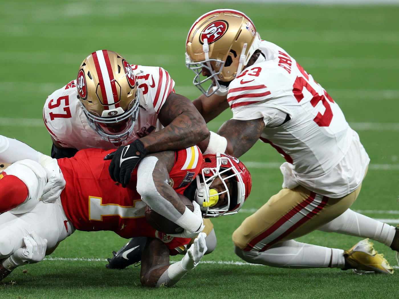  壁紙 — 三藩市四九人隊的兩名防守球員在激烈的NFL美式足球比賽中，於充滿活力的綠色球場上擒抱堪薩斯城酋長隊的一名球員。