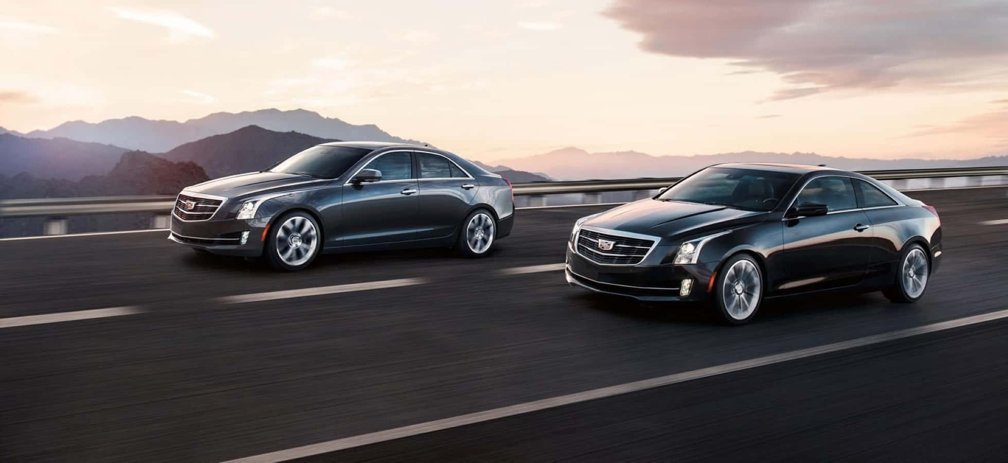 Cadillac Ats 桌布 壁紙 — 兩輛時尚的Cadillac汽車在日落餘暉中的山脈高速公路上並排行駛。