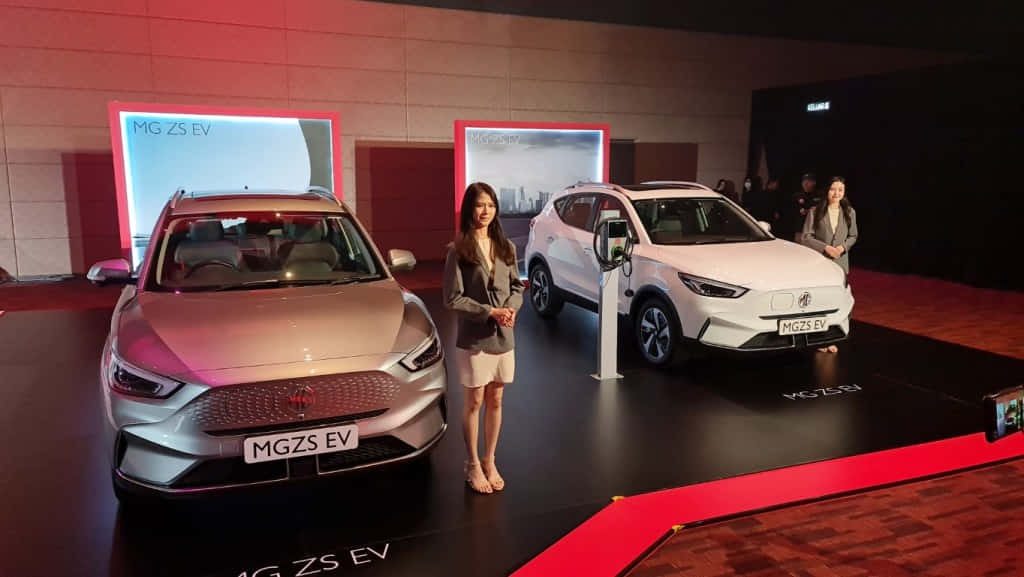  壁紙 — 兩輛時尚的MG ZS EV電動車在紅地毯舞台上，主持人在旁，在戲劇性燈光下展示。