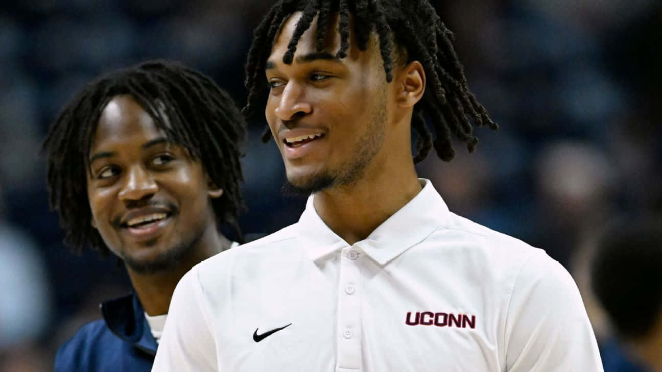  壁紙 — 兩位身穿UConn Polo衫的籃球運動員在球場上分享時刻，身後有模糊的觀眾。