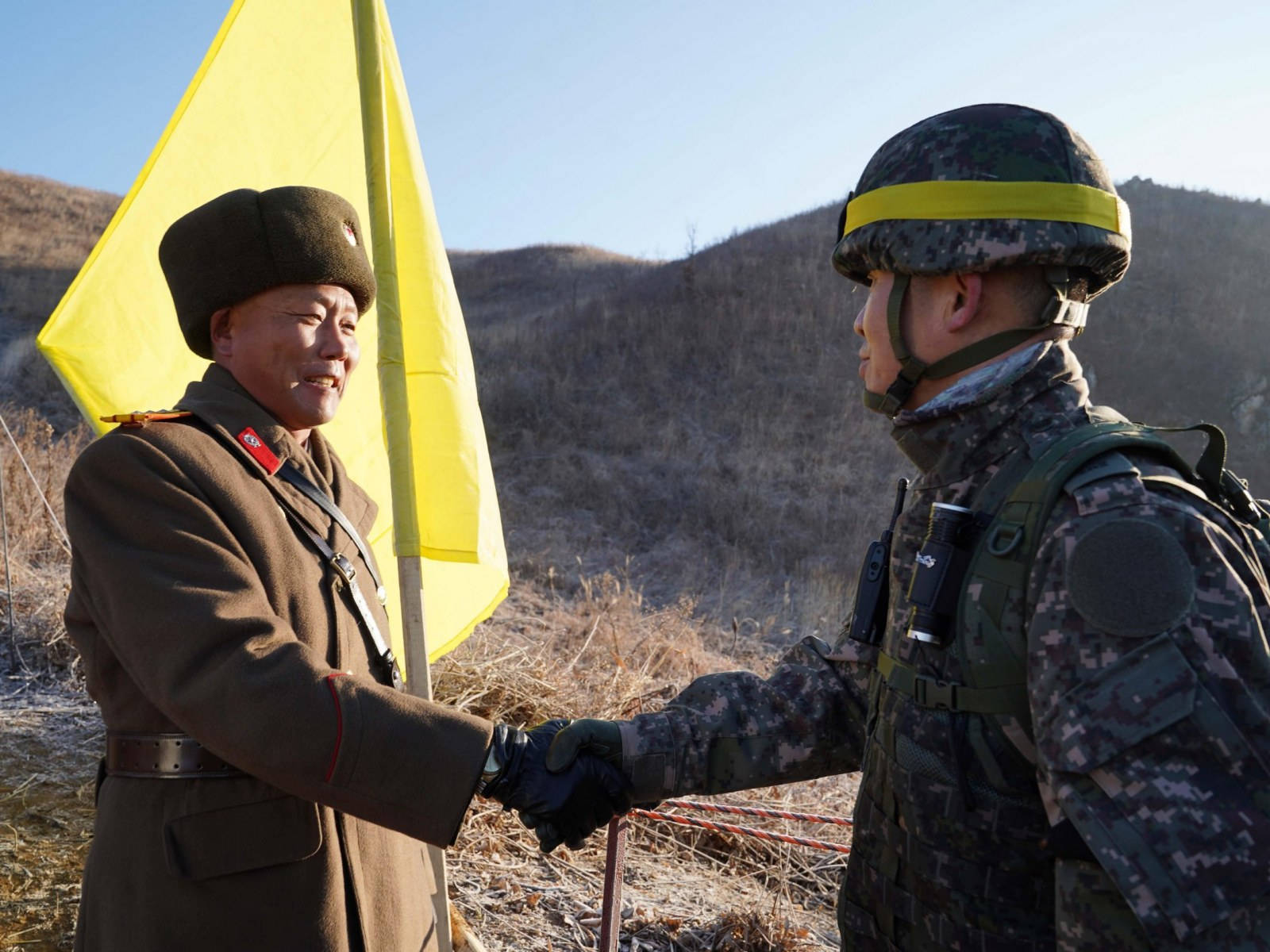 兩名士兵喺乾燥風景中，喺有黃色旗幟嘅邊境握手。
