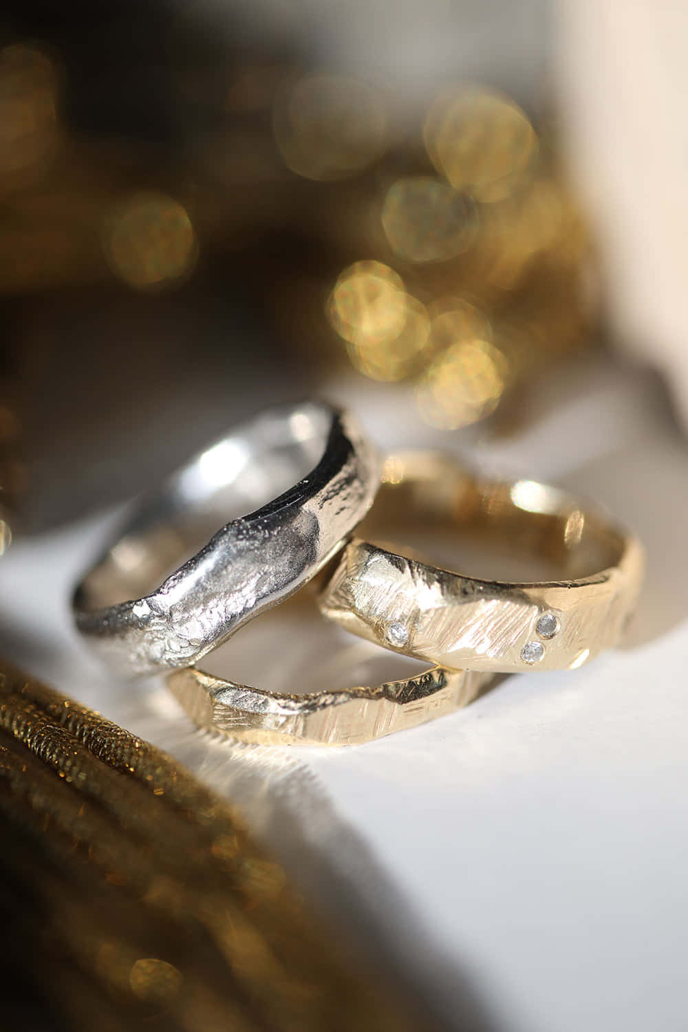 兩隻帶紋理的結婚戒指，一金一銀，放在白色表面上，背景為金色散景。