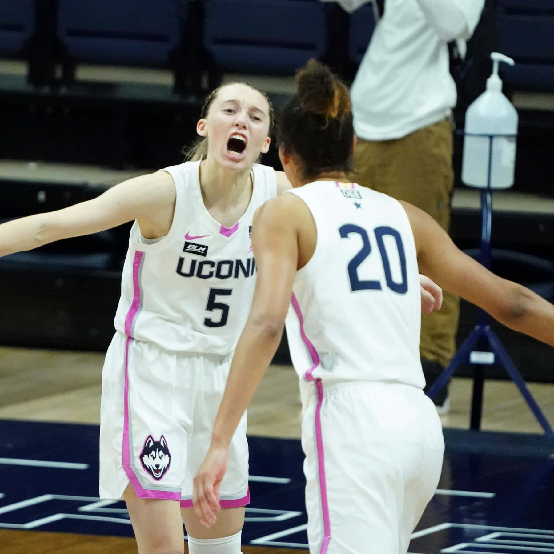  壁紙 — 兩名身穿白色球衣的UConn女子籃球運動員在球場上張開雙臂、張開嘴巴，激烈慶祝。