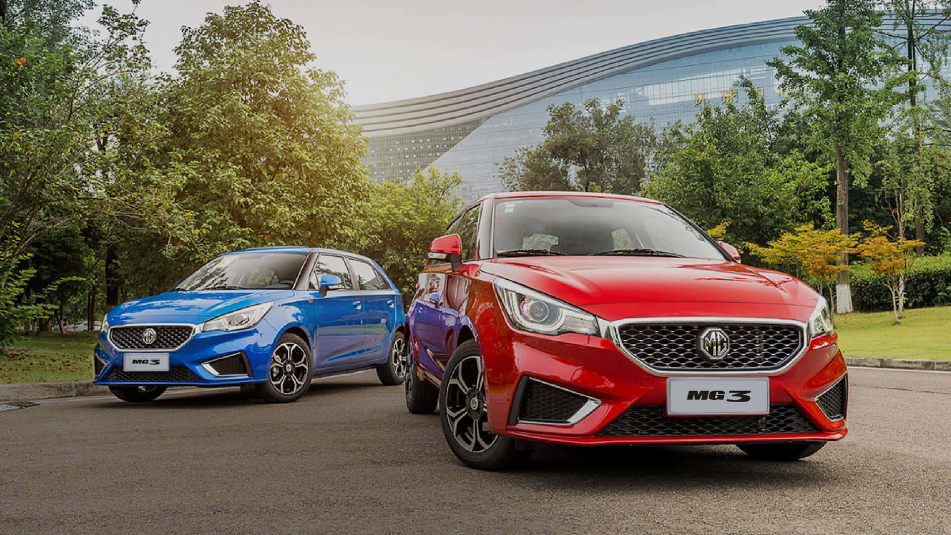 Mg 3 桌布 壁紙 — 兩輛充滿活力的MG3汽車，藍色和紅色，停在瀝青路上，背景是現代玻璃建築和綠樹。