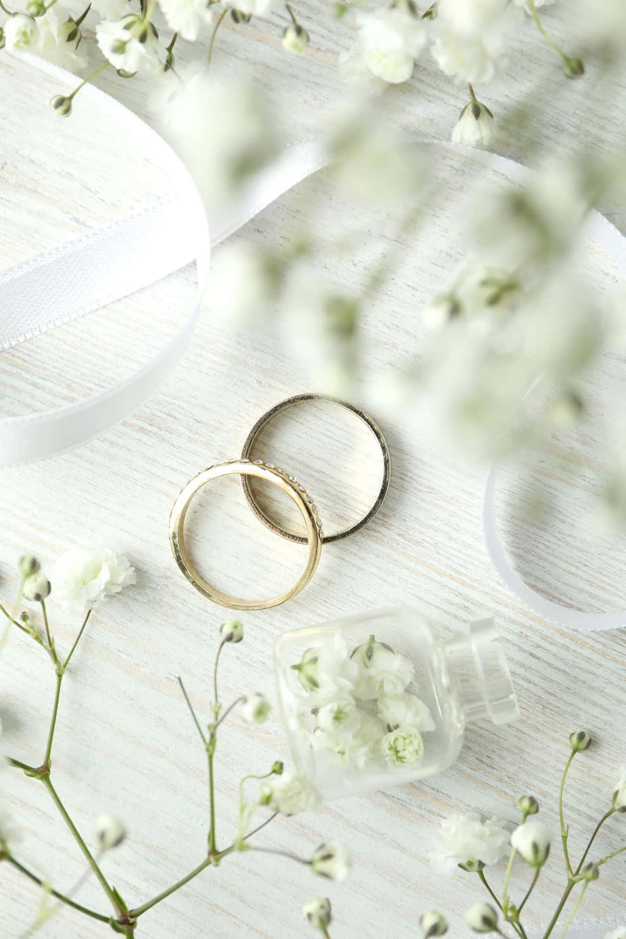 白色木質表面上的兩枚金色結婚戒指，搭配滿天星和絲帶。