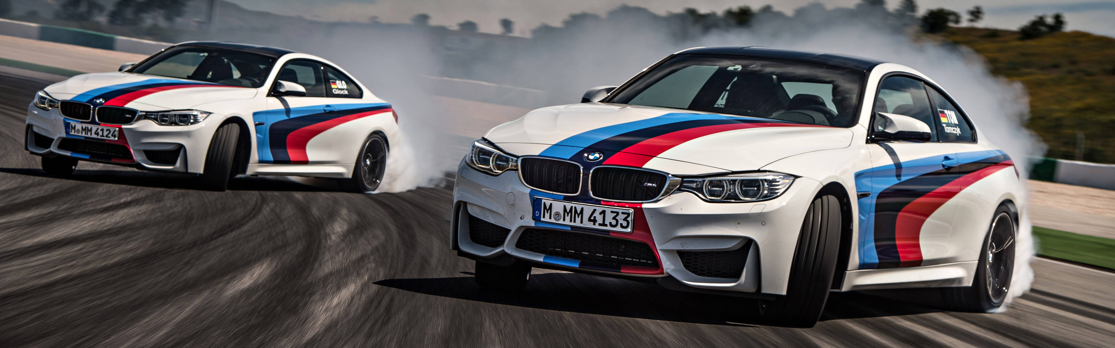 兩輛BMW M4賽車在賽道上漂移，身後留下煙霧。