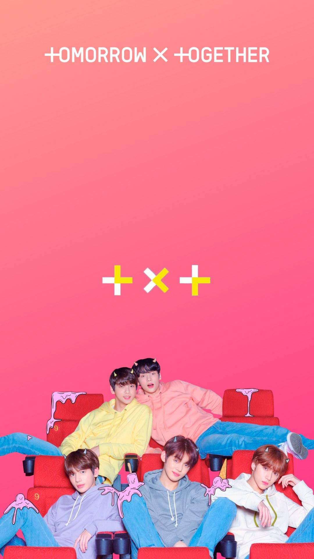 TXT 坐在電影椅上 壁紙 — 五個穿著彩色連帽衫的年輕男子，在充滿活力的粉紅色漸變背景前，懶洋洋地靠在紅色電影院座位上。