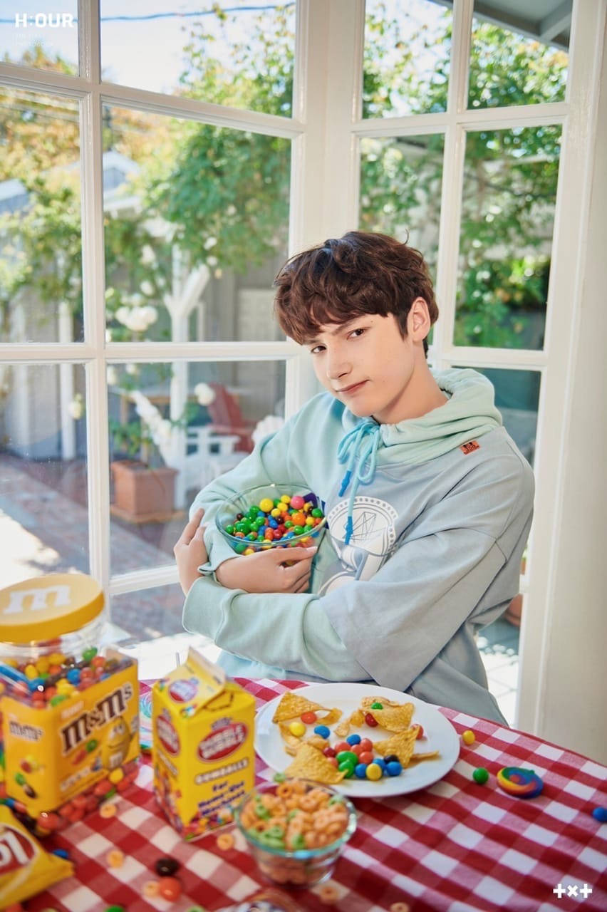年輕男子在窗邊擺滿糖果的桌上手持一碗M&M's。