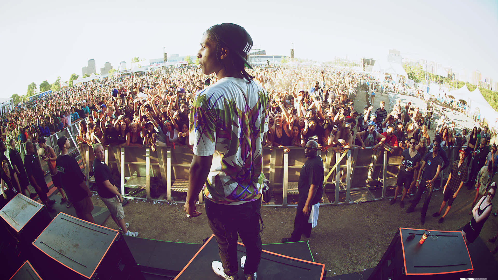 嘻哈傳奇 Tyler, The Creator 與 Asap Rocky 壁紙 — 一位表演者站在舞台上，面對著戶外音樂節上在明亮日光下歡呼的龐大群眾。