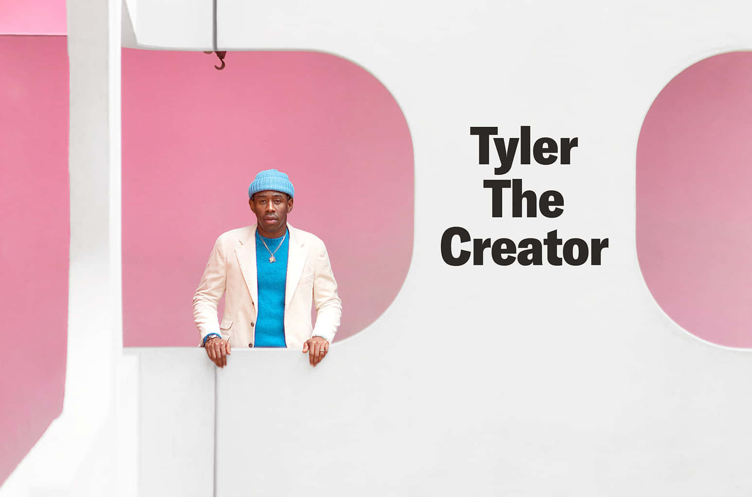 tyler the creator 桌布 壁紙 — Tyler The Creator 靠喺一個白色邊緣上，對住一個大膽嘅粉紅同白色幾何牆，牆上以黑色字體寫住佢個名。
