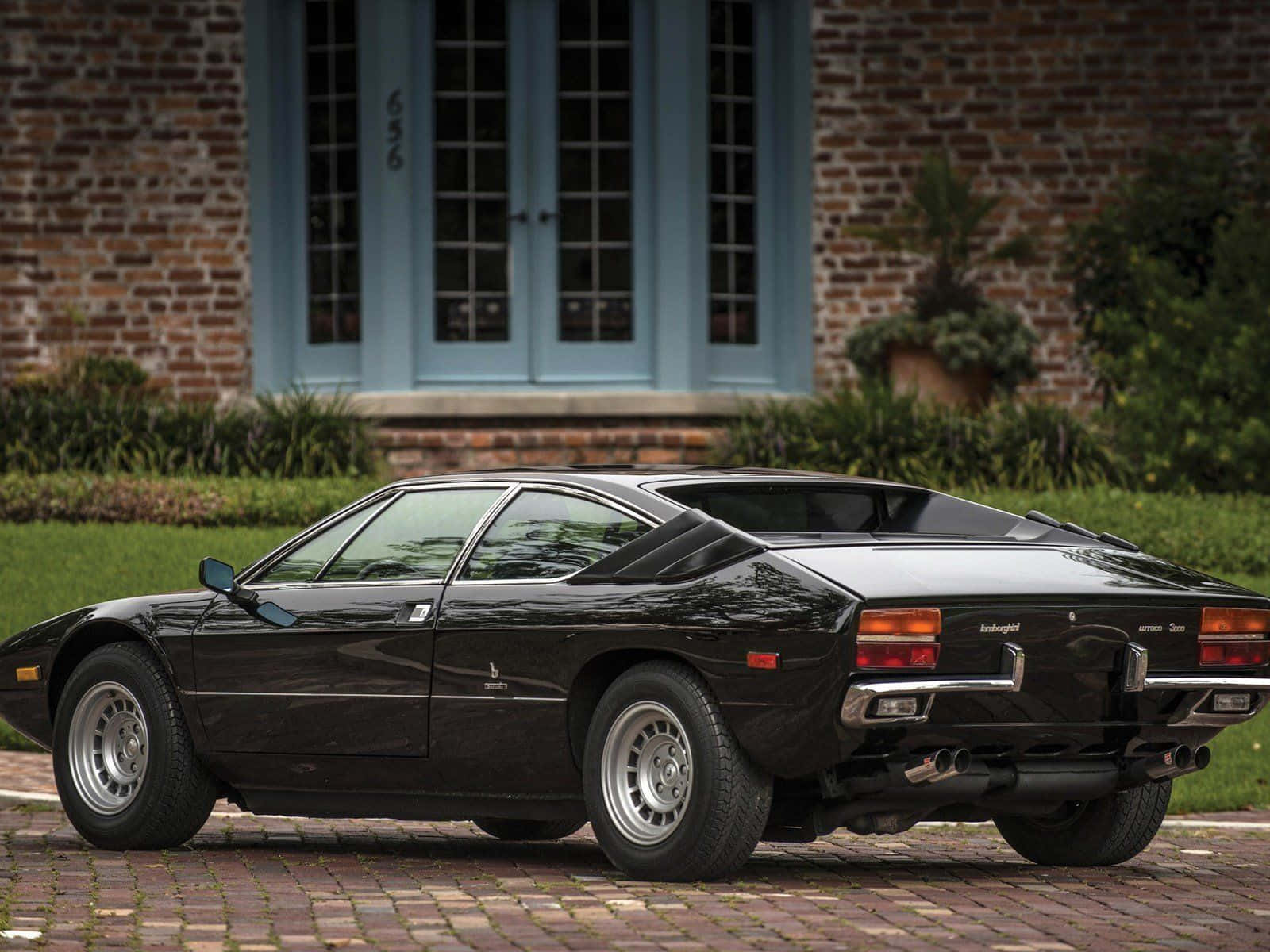 Lamborghini Urraco 桌布 壁紙 — 一架型格黑色林寶堅尼Countach停泊在磚砌車道上，前面是間有藍色門的磚屋。