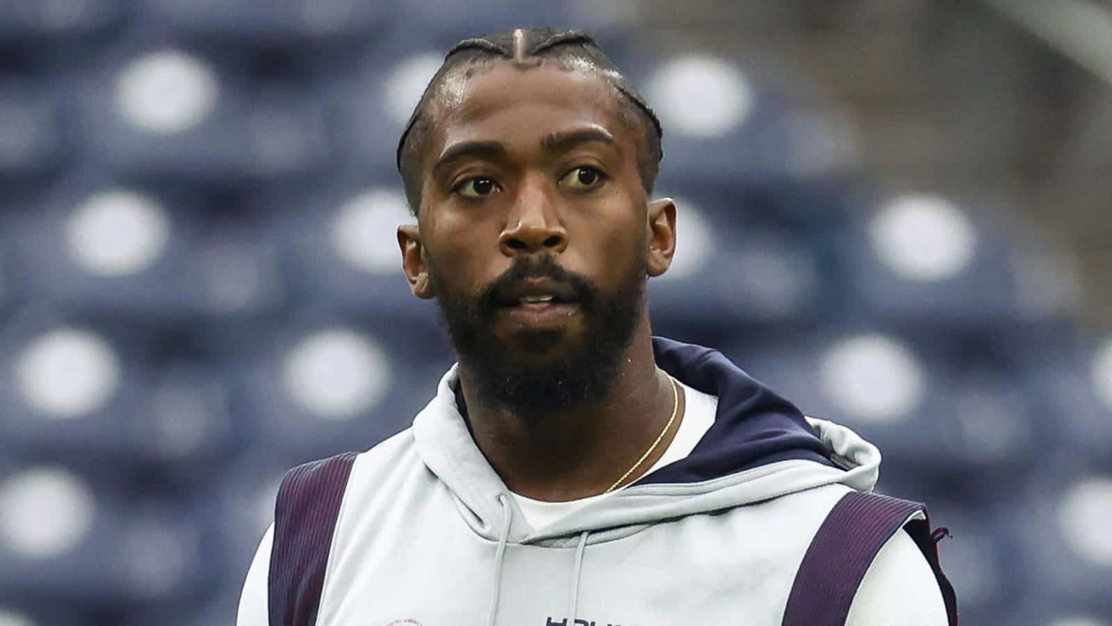 Tyrod Taylor專注暖身 壁紙 — 一位專注的運動員，編著辮子頭髮和鬍鬚，穿著白色和紫色的連帽衫，背景是模糊的體育場座位。