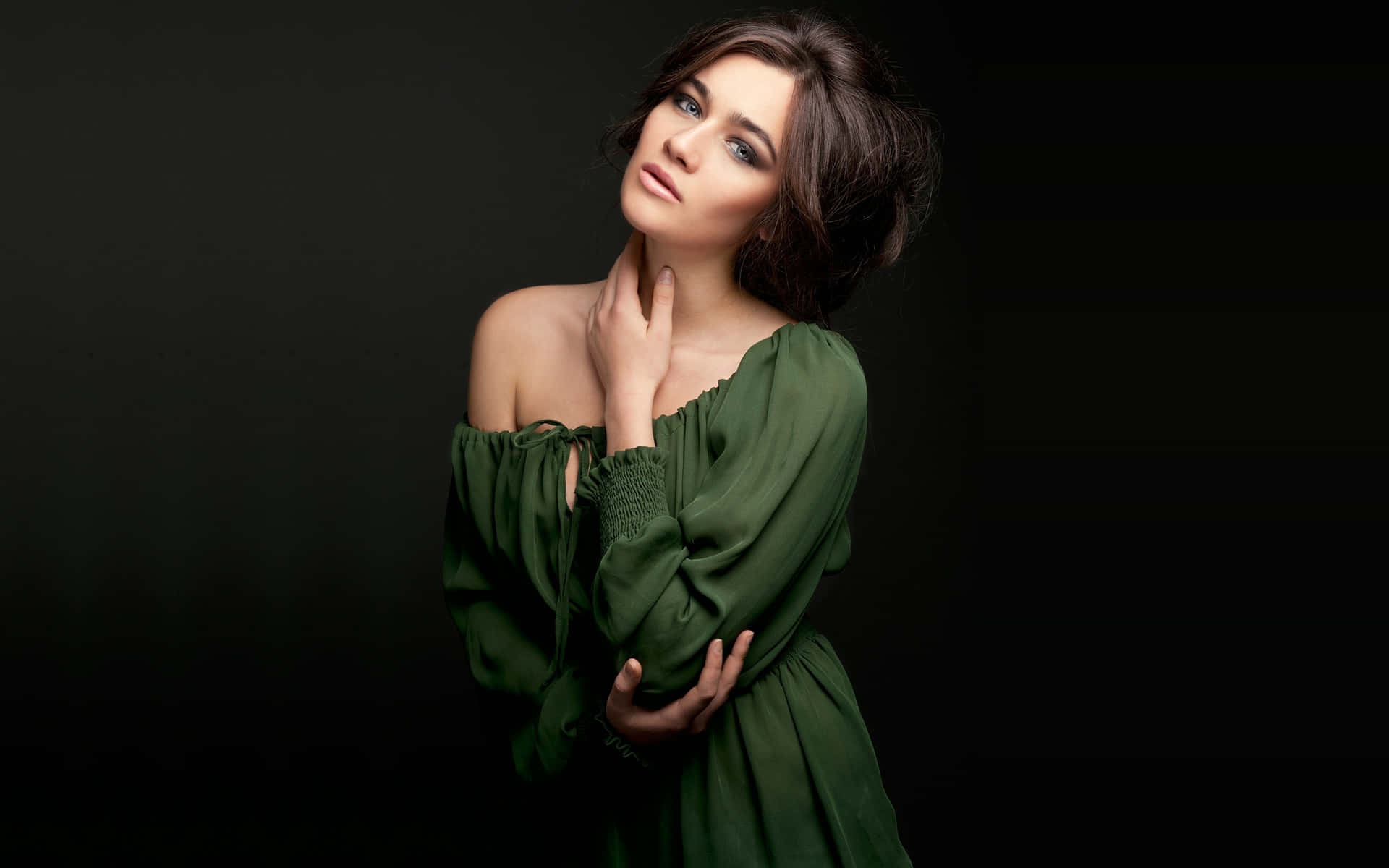 一位身穿綠色連衣裙的女性在深色背景前，一手放在脖子上擺姿勢。