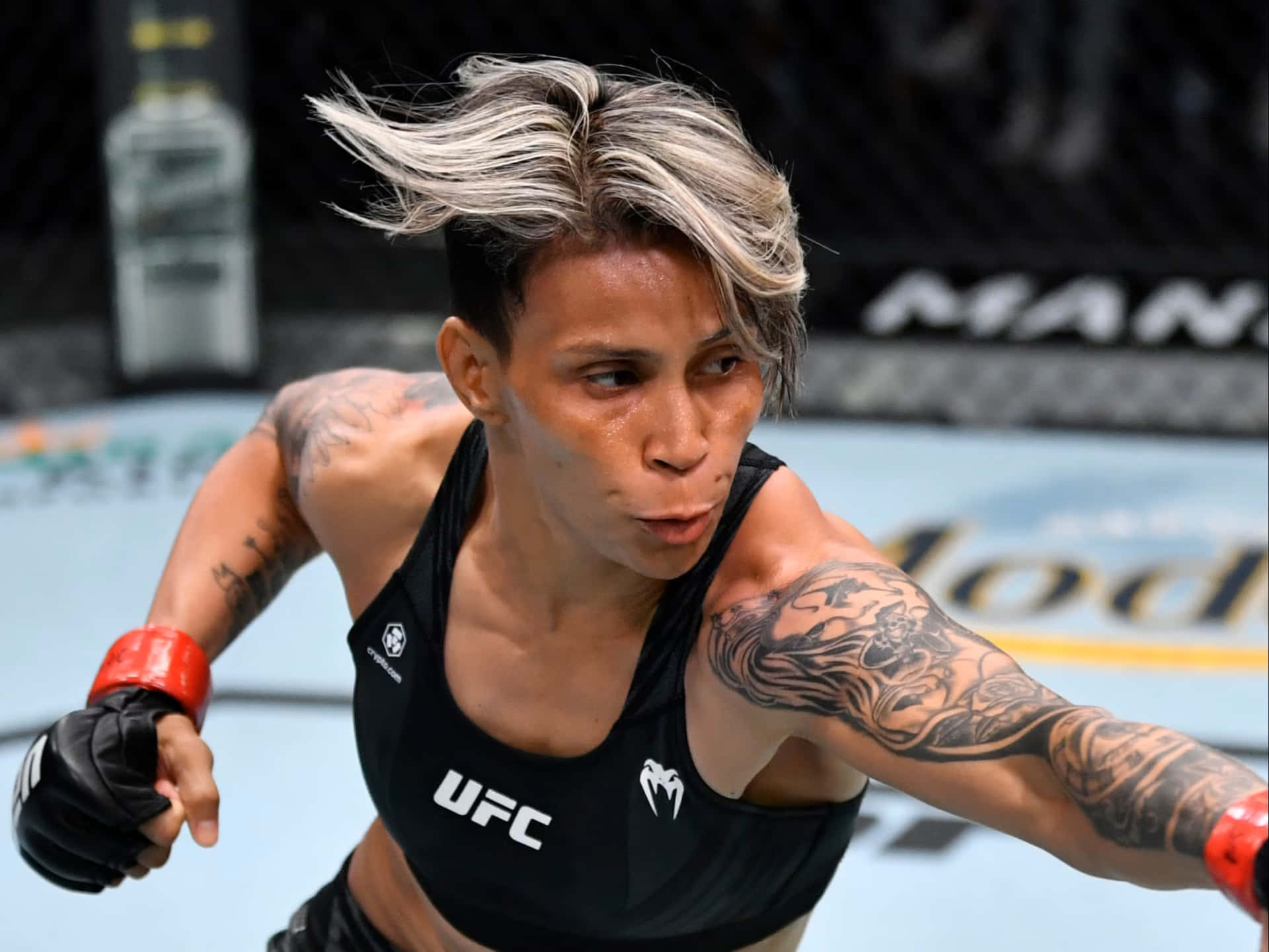  壁紙 — 一位有紋身和風吹亂頭髮的女MMA拳手在UFC八角籠中激烈比賽時向前猛衝。