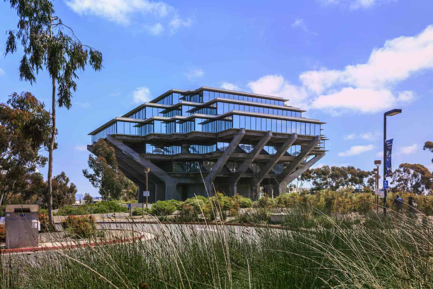 UCSD 圖書館遠景 壁紙 — 一座引人注目的現代玻璃和混凝土建築，帶有階梯式陽台，矗立在晴朗的藍天下，飄著蓬鬆的白雲。