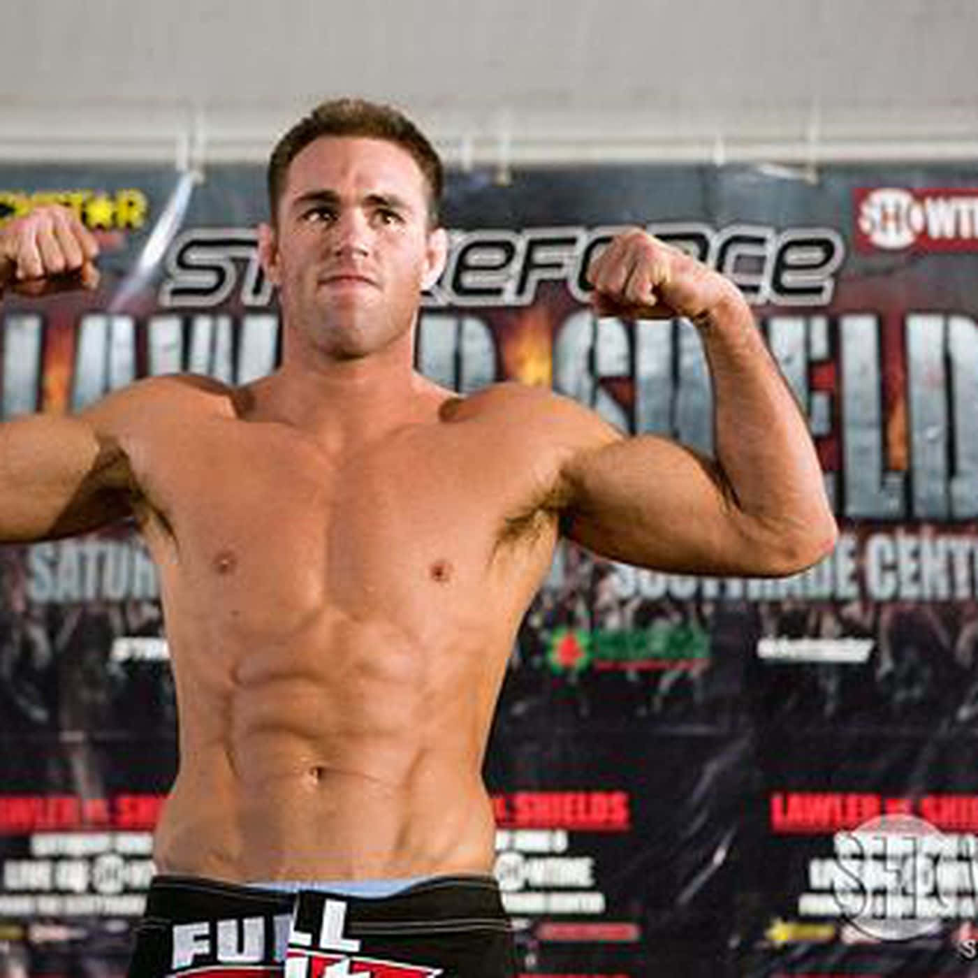 傑克·希爾茲於UFC 150賽事 壁紙 — 一個肌肉發達、赤裸上身的戰士在摔角活動橫幅前繃緊手臂和軀幹。