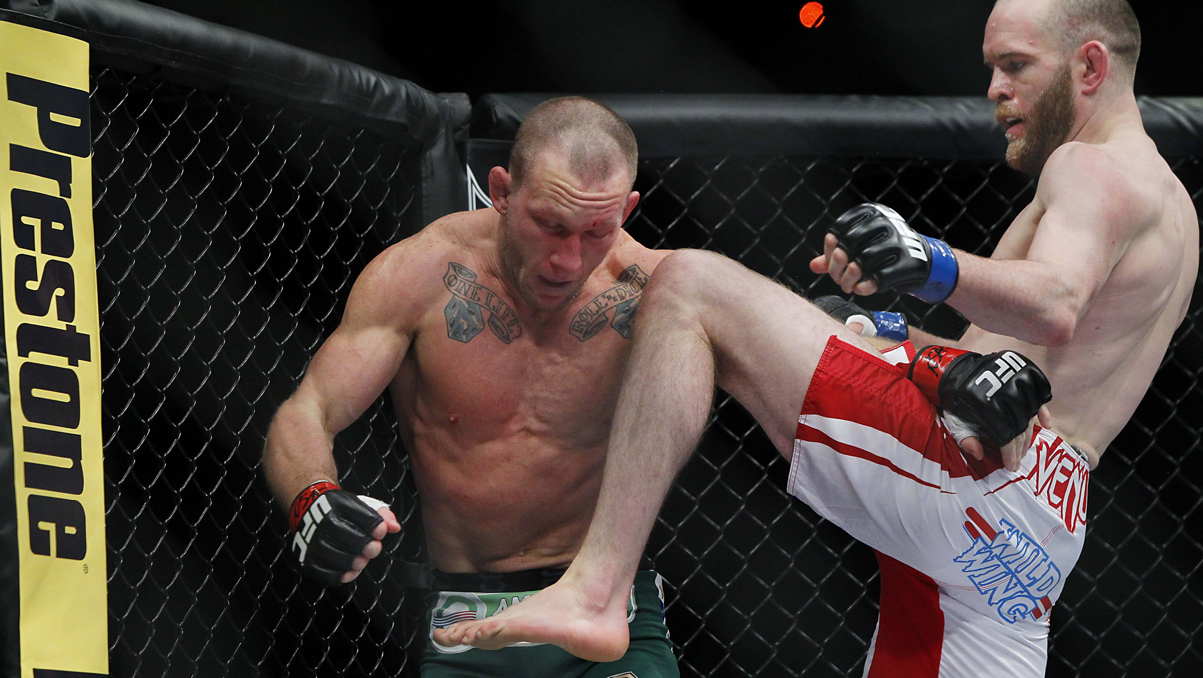 UFC 160 格雷·梅納德遭T.J. 格蘭特膝擊 壁紙 — 一名拳手在明亮的場館燈光下，於UFC八角籠內向對手施展高踢。