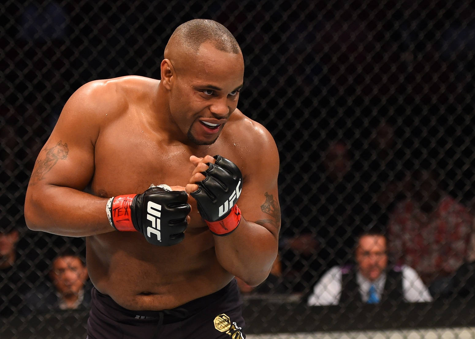 UFC 226 丹尼爾·科爾米爾 壁紙 — 一位肌肉發達的UFC拳手在八角籠內咧嘴大笑，背景是鐵絲網後模糊的觀眾。